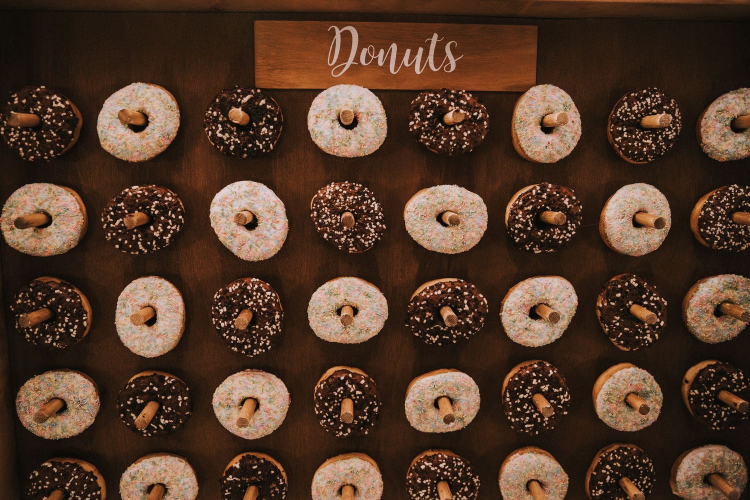 Donut wall display with chocolate and powdered donuts arranged in rows with wooden Donuts sign.