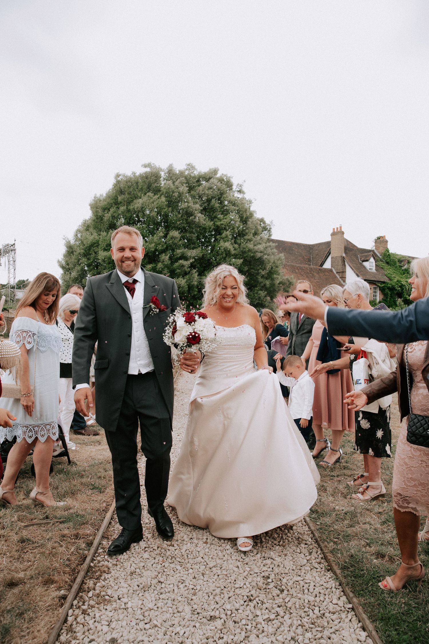 Bride and groom walk hand in hand through cheering guests tossing confetti at outdoor wedding.