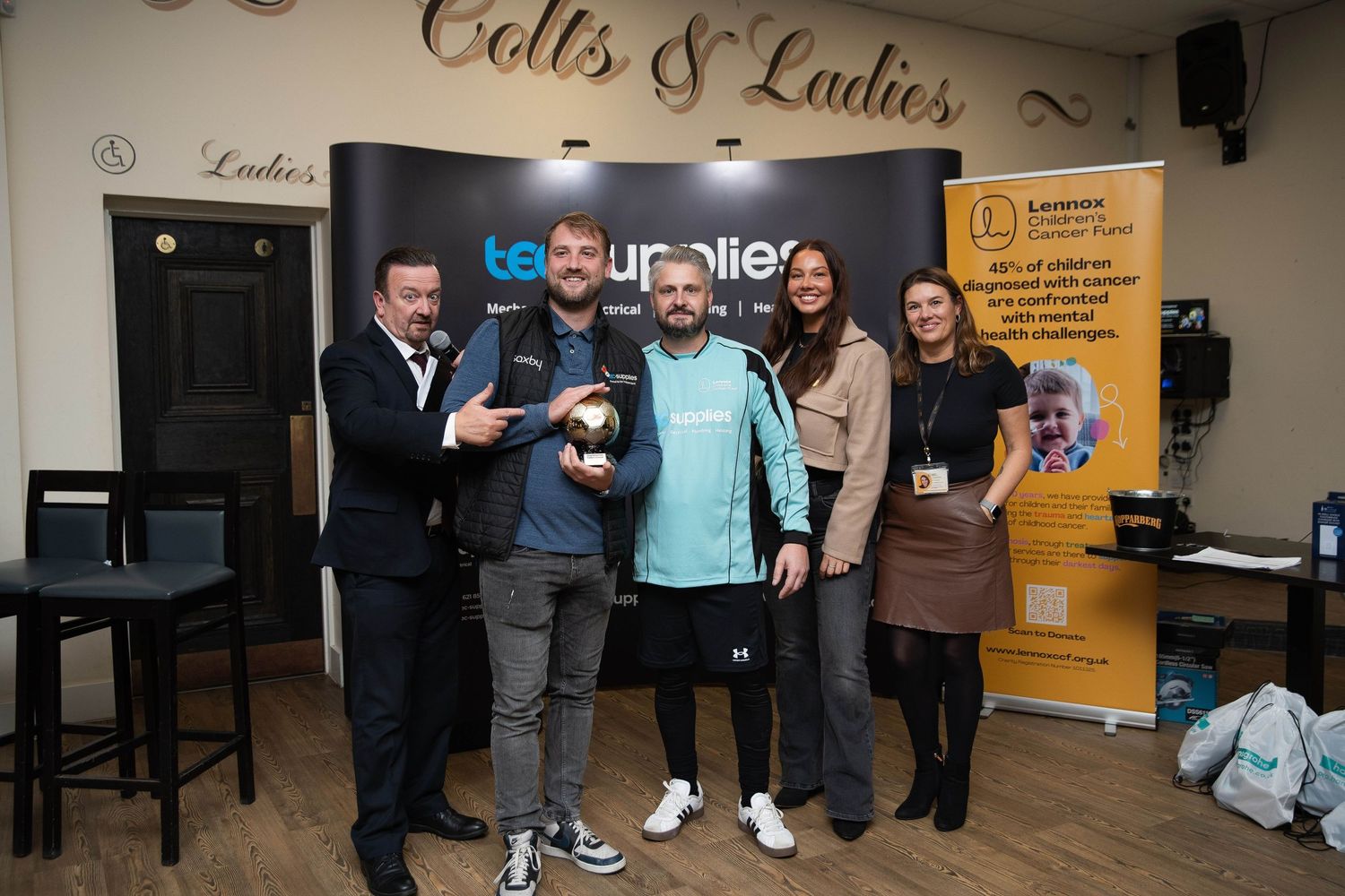 Five people stand together, one holding a trophy at a corporate fundraising event in Basildon Essex.