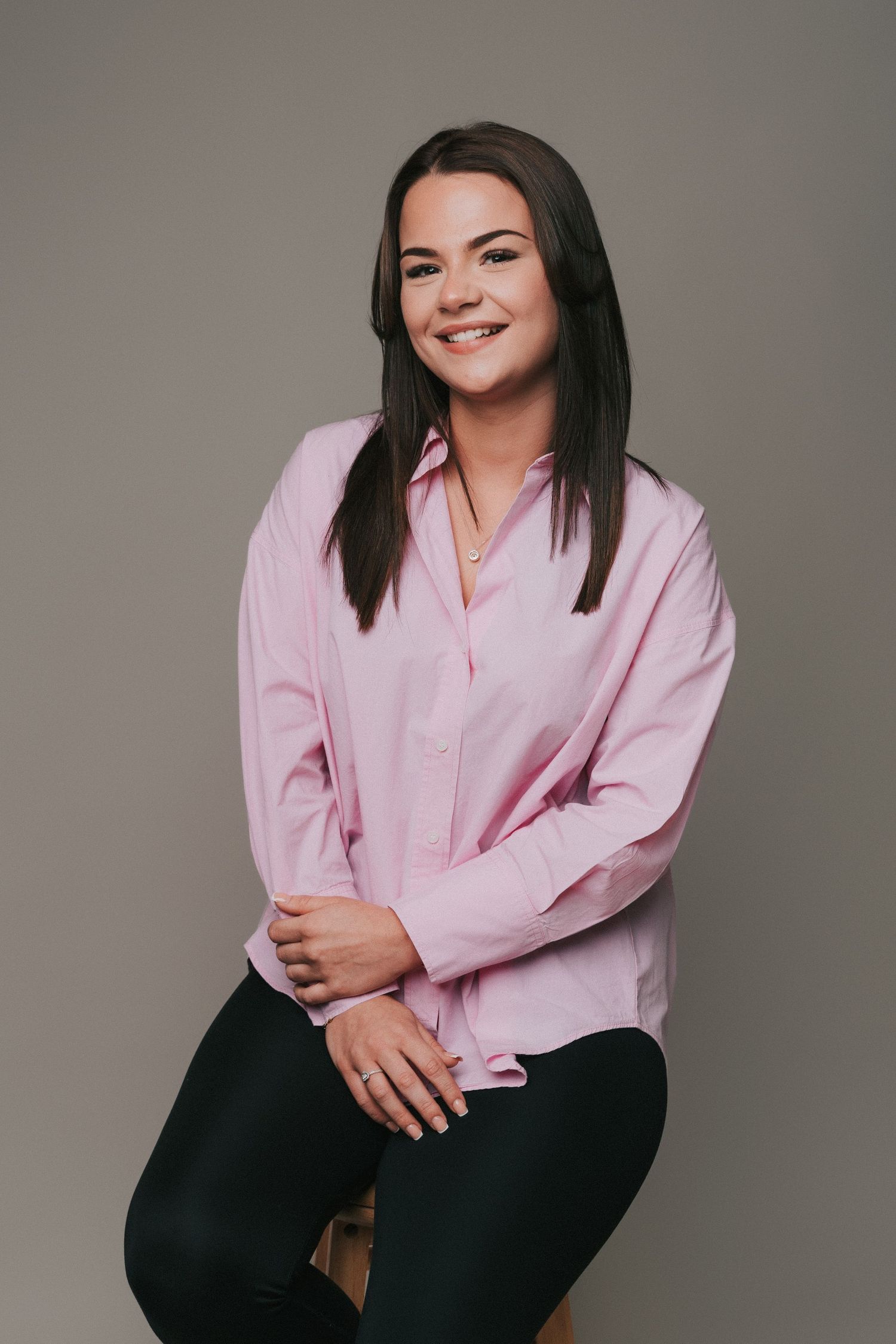 A young woman wearing a light pink button-up shirt, smiling at the camera, perfect for professional headshots in Basildon, Essex