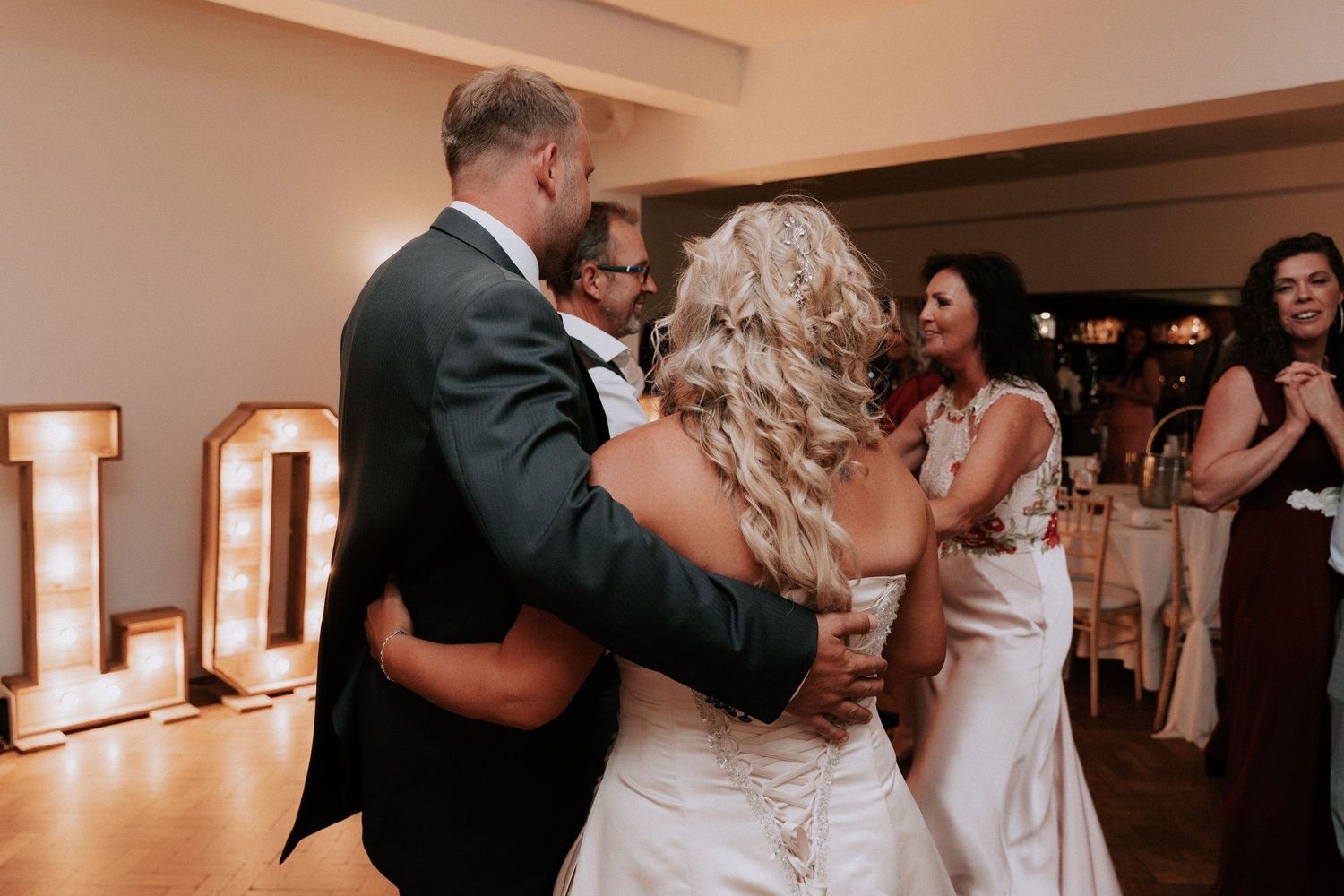 Bride and groom share first dance at wedding reception with illuminated LOVE letters in background.