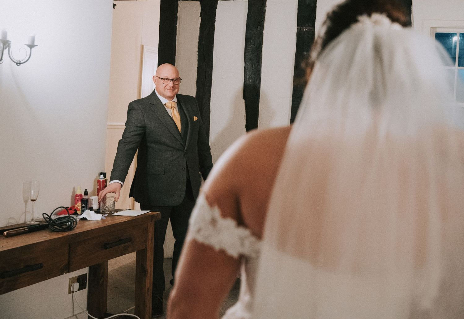 Father of the bride seeing daughter in wedding dress for the first time in a rustic Tudor-style room.