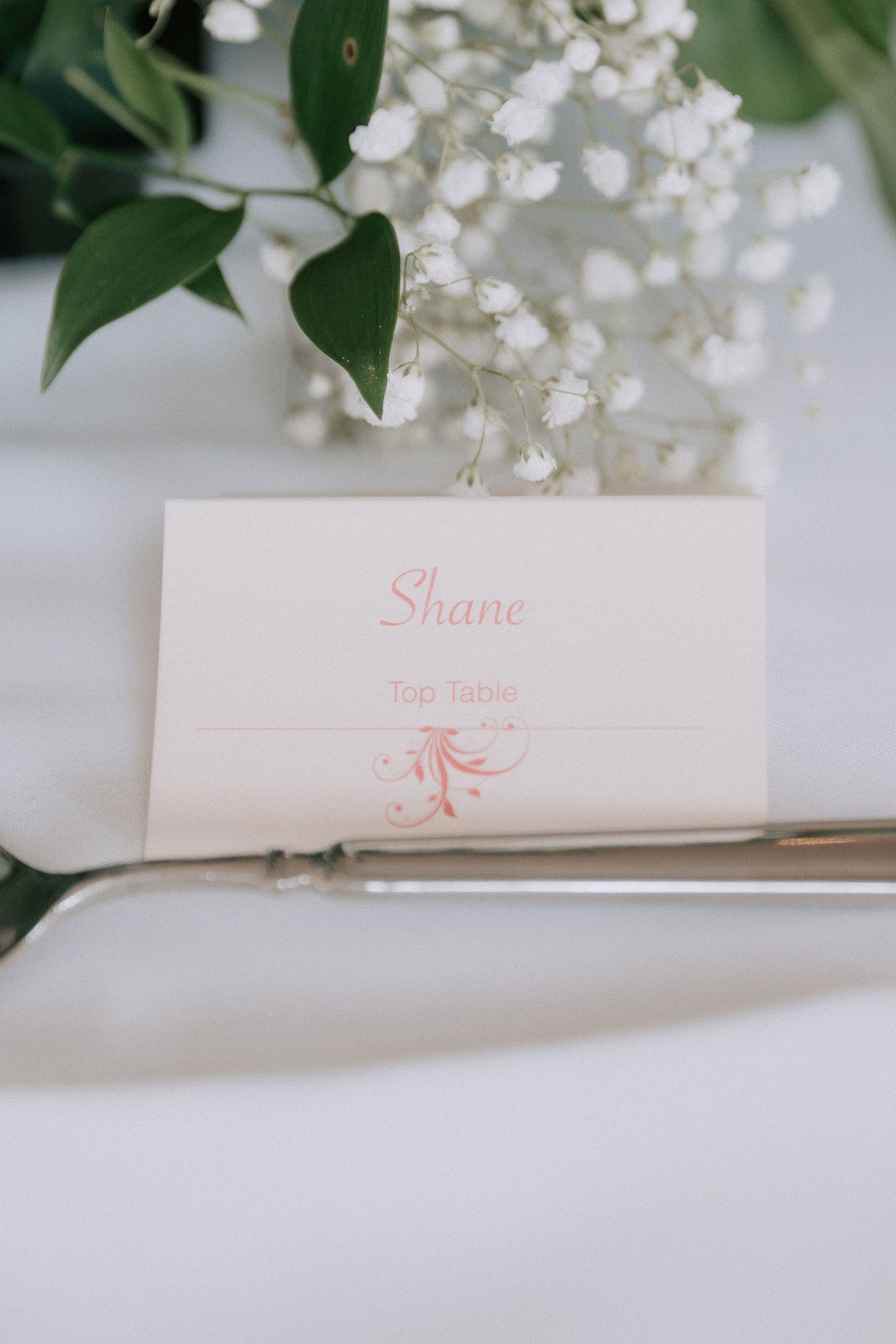 Elegant wedding place card for Shane at the Top Table, displayed with baby's breath flowers on a silver charger plate.