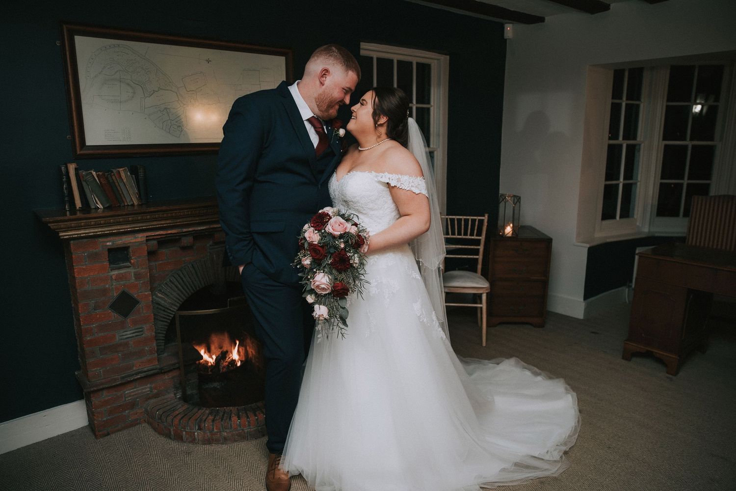 Bride and groom sharing a romantic moment by a glowing fireplace, bride holding a beautiful bouquet.