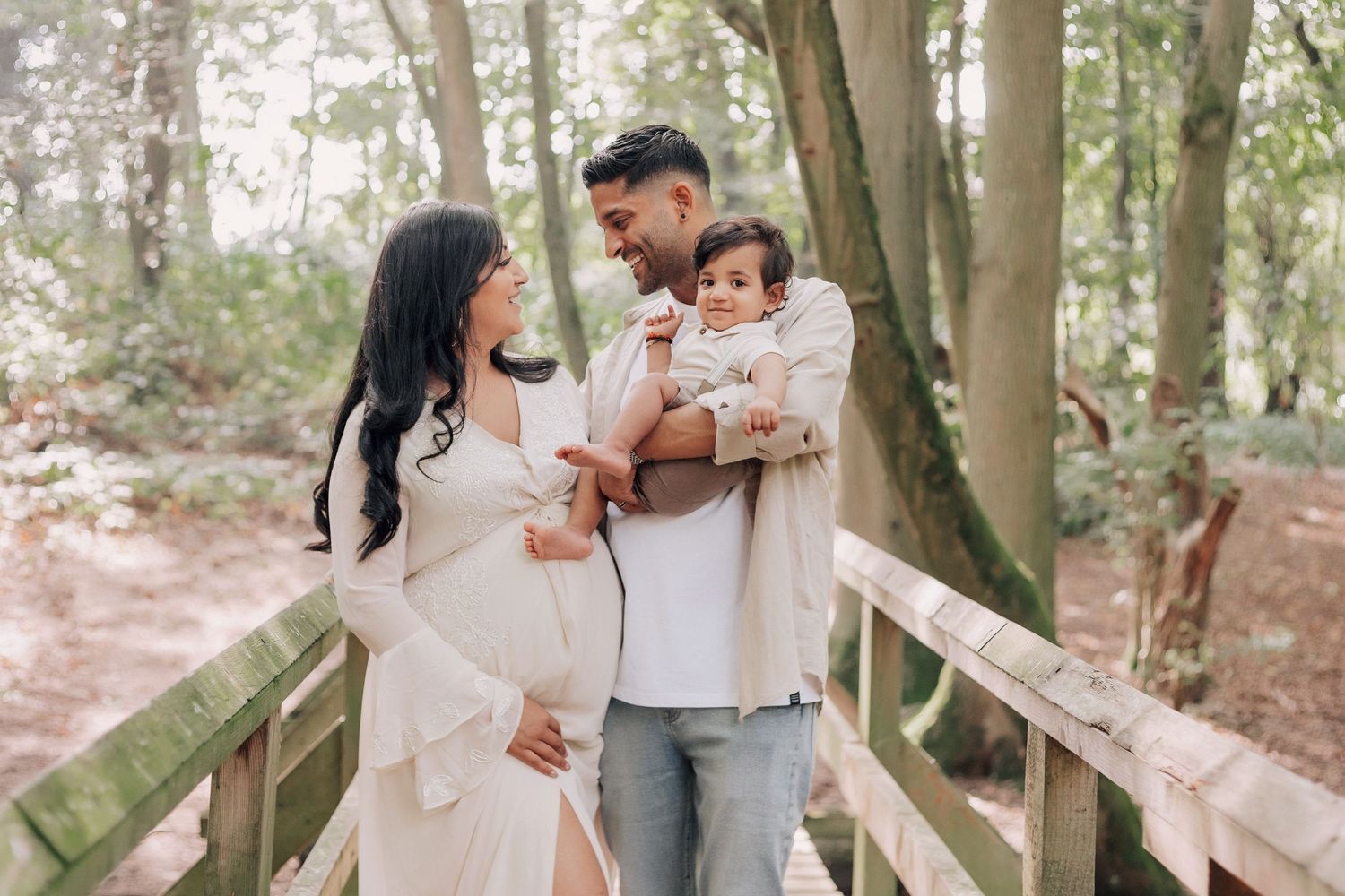 family of 3 pregnant mother and father lovingly looking at each other eldest boy child smiling wearing white at Wesley h