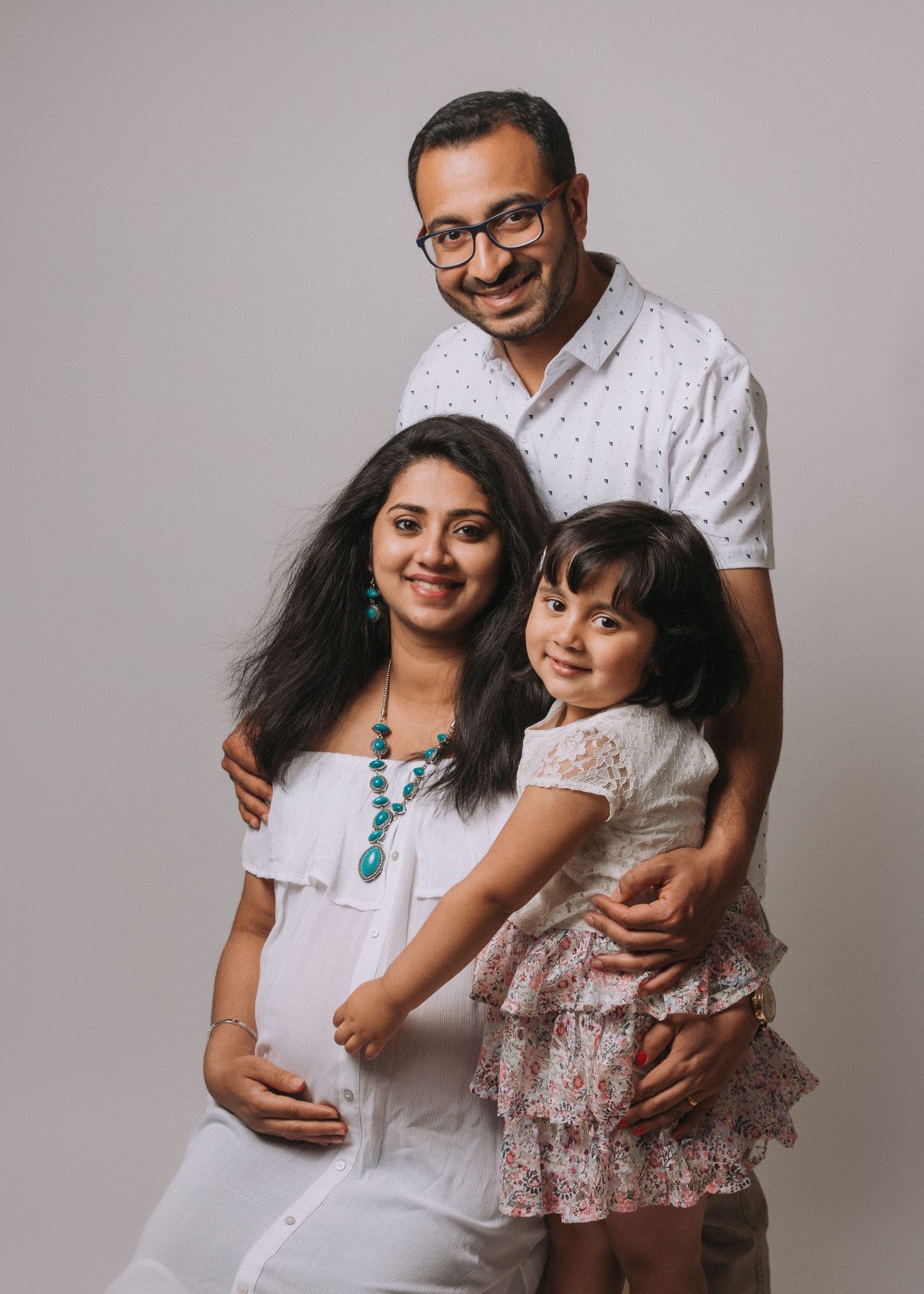 family of 3 pregnant mother and father with eldest child smiling wearing white