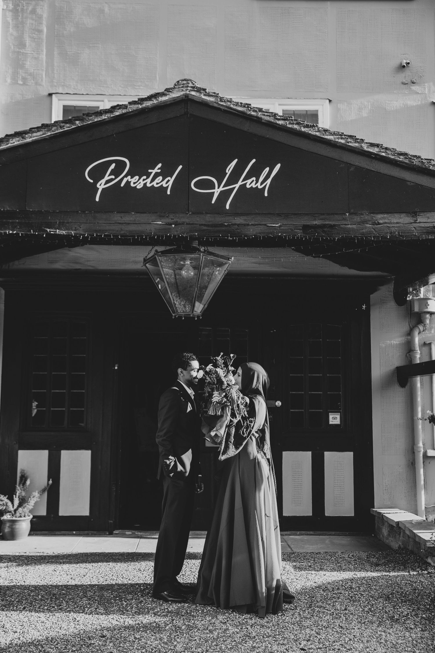 Black and white photo of a couple kissing in front of Prested Hall wedding venue entrance.