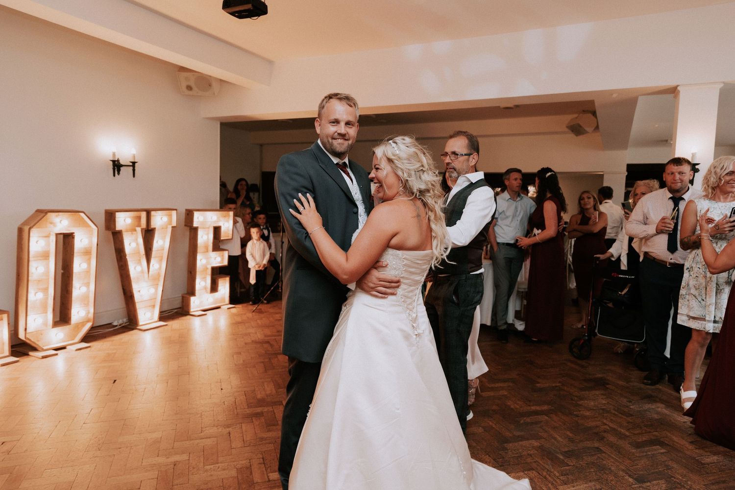 Bride and groom share first dance in front of illuminated LOVE letters at elegant wedding reception.