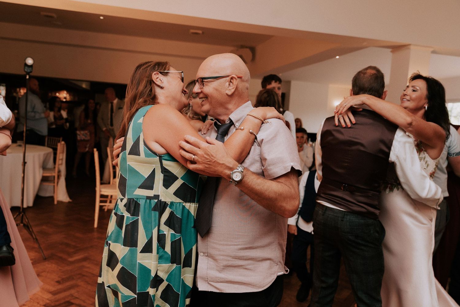 Guests dancing and embracing joyfully at an indoor wedding reception celebration.