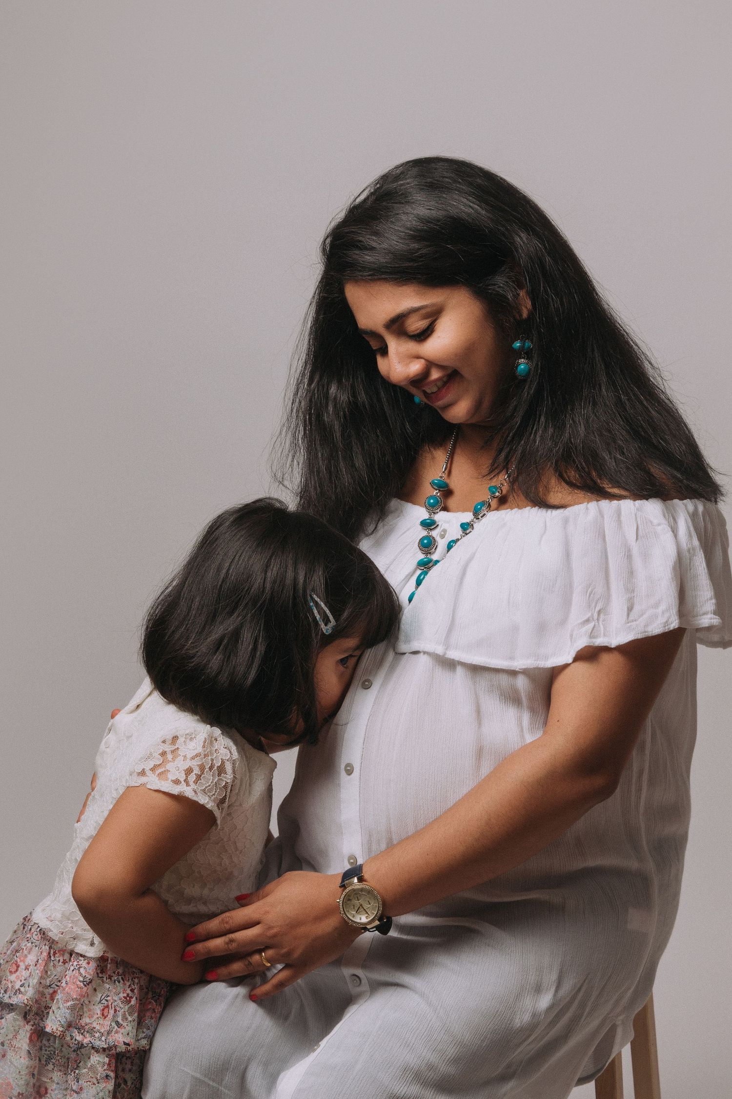 A series of intimate portraits showing a tender embrace between two people in white clothing against a gray background.