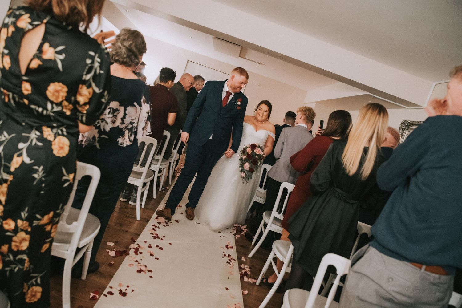 Newlyweds walk back down the aisle together after their wedding ceremony as guests look on and celebrate.