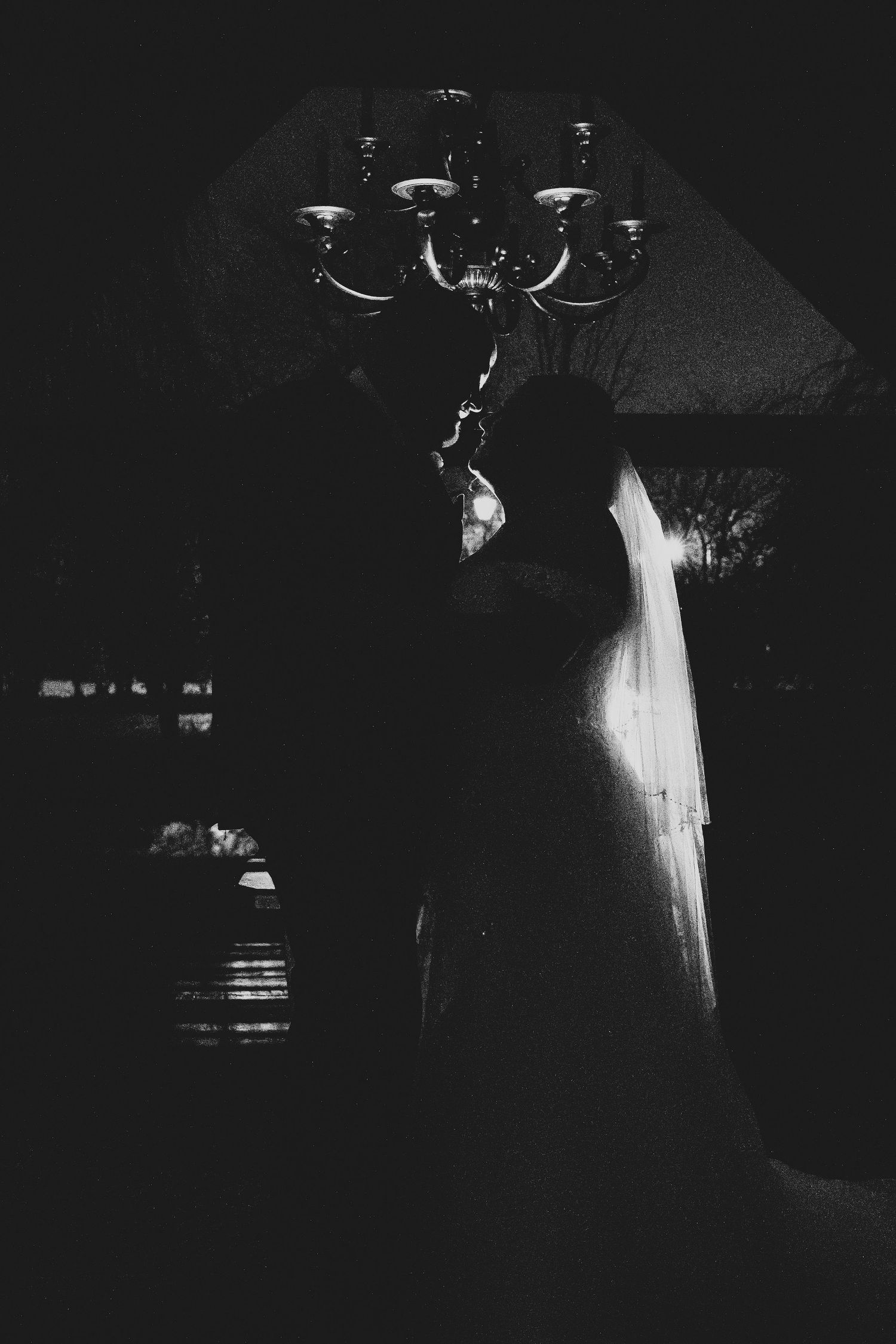 Romantic black and white silhouette of bride and groom kissing beneath an elegant chandelier.