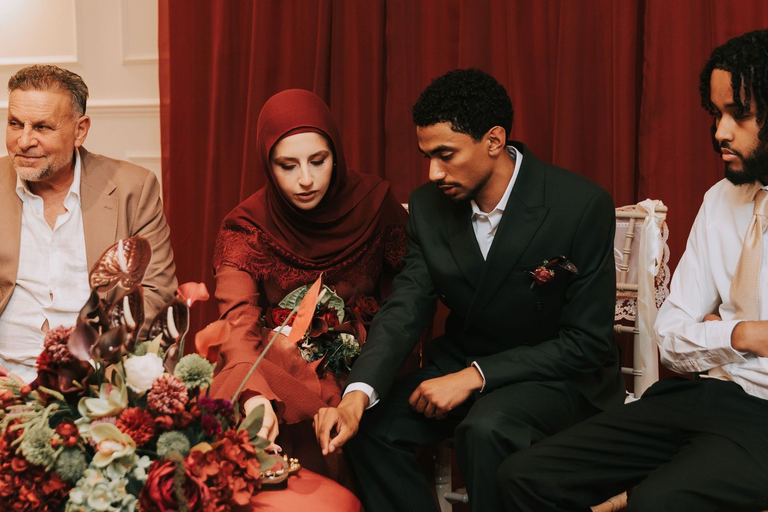 A Muslim couple in formal attire sit together at an elegantly decorated table during a wedding ceremony.
