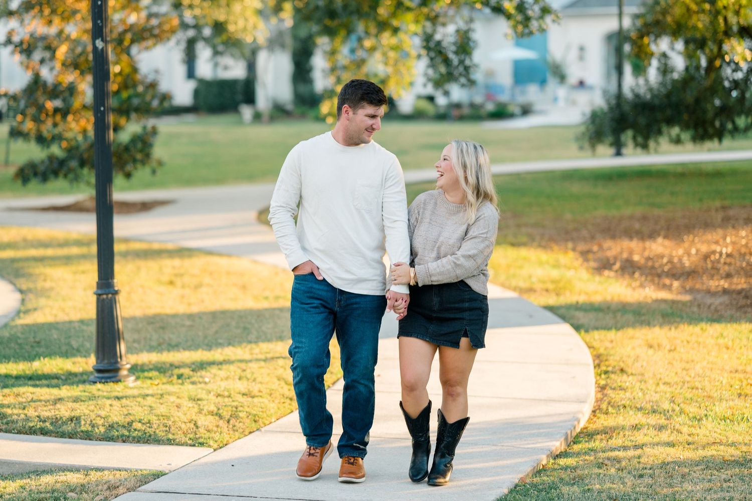 A couple walks together on a path during golden hour with autumn leaves scattered on the ground.