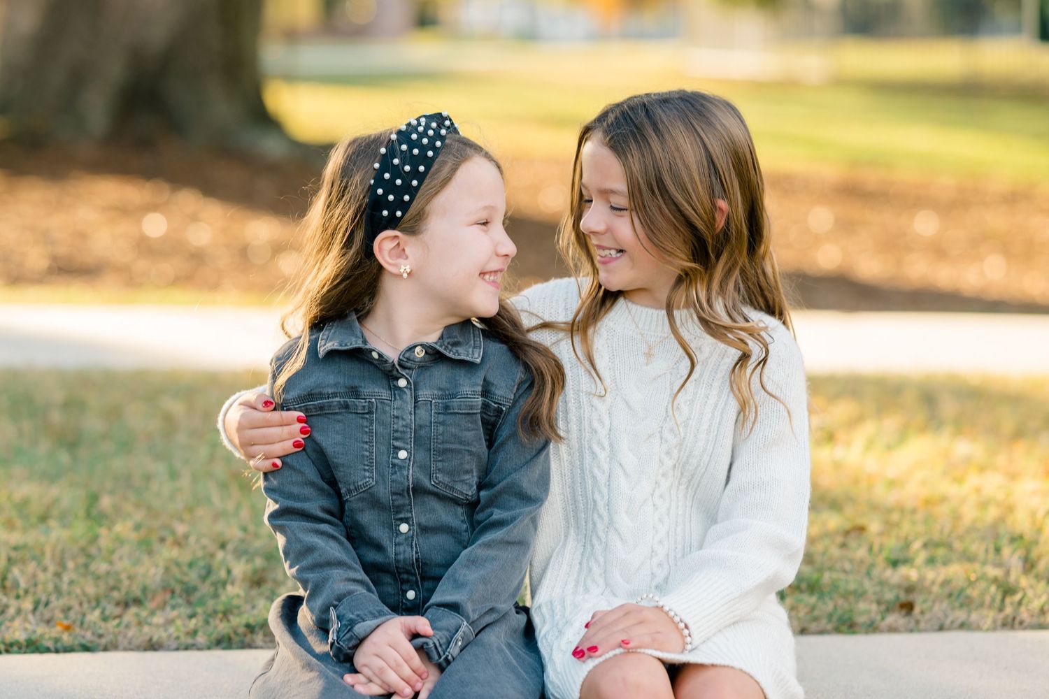 Two people sit together outdoors in autumn wearing coordinating denim and cream colored outfits.