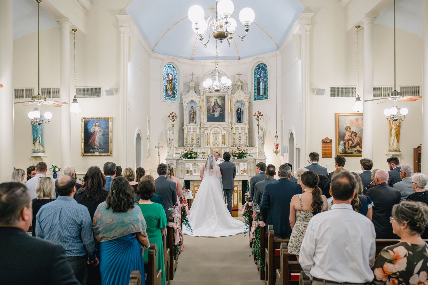 Wedding ceremony in a beautiful Catholic church with guests seated in pews as bride and groom stand at the altar.
