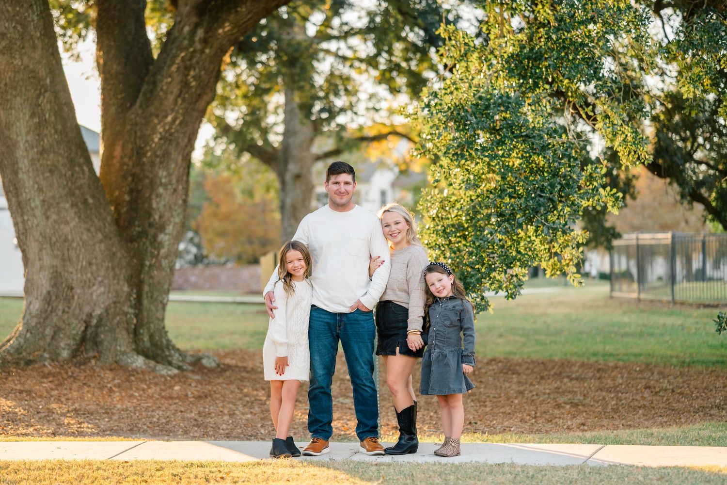 A family walks together under large oak trees during a golden autumn afternoon photoshoot.