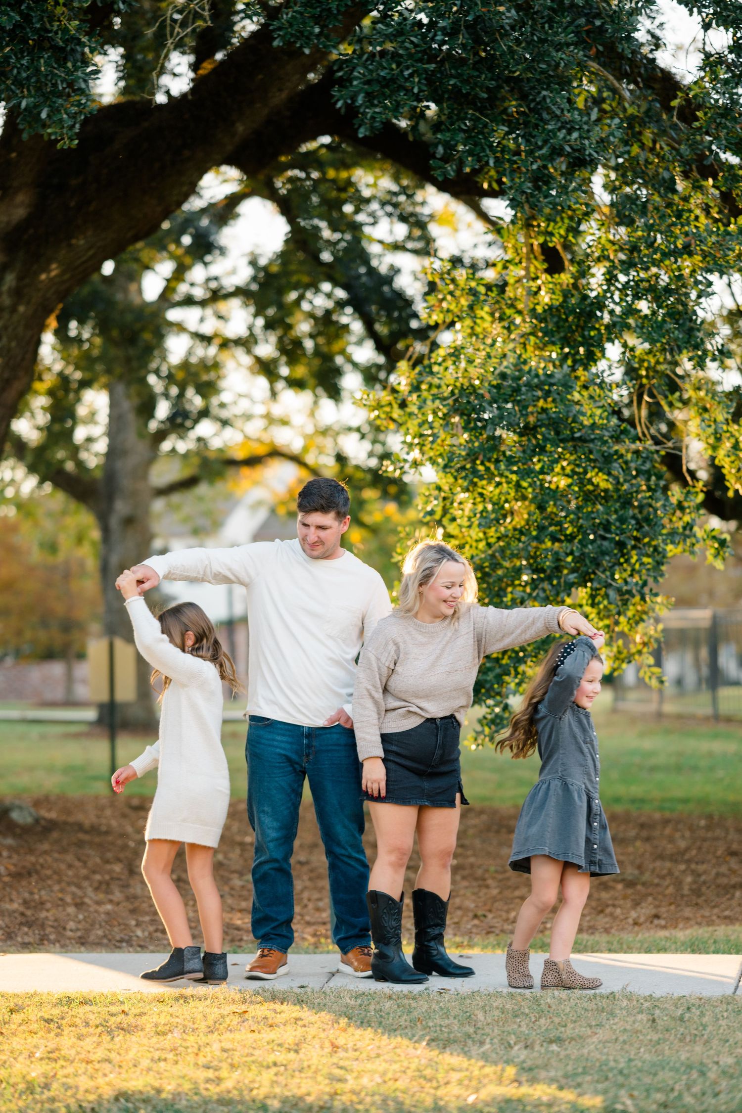 A group of friends balance together on a curb in a sunny park during golden hour, surrounded by lush trees.
