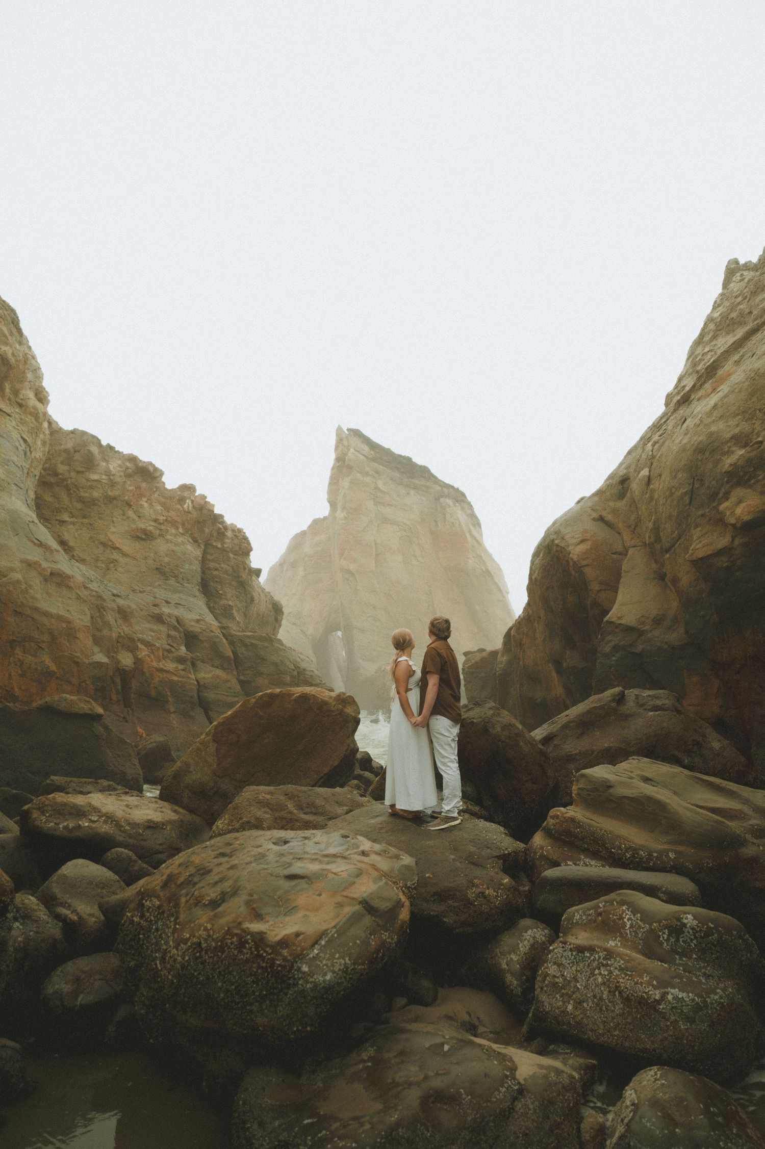 Wedding couple standing among dramatic rocky coastal formations.