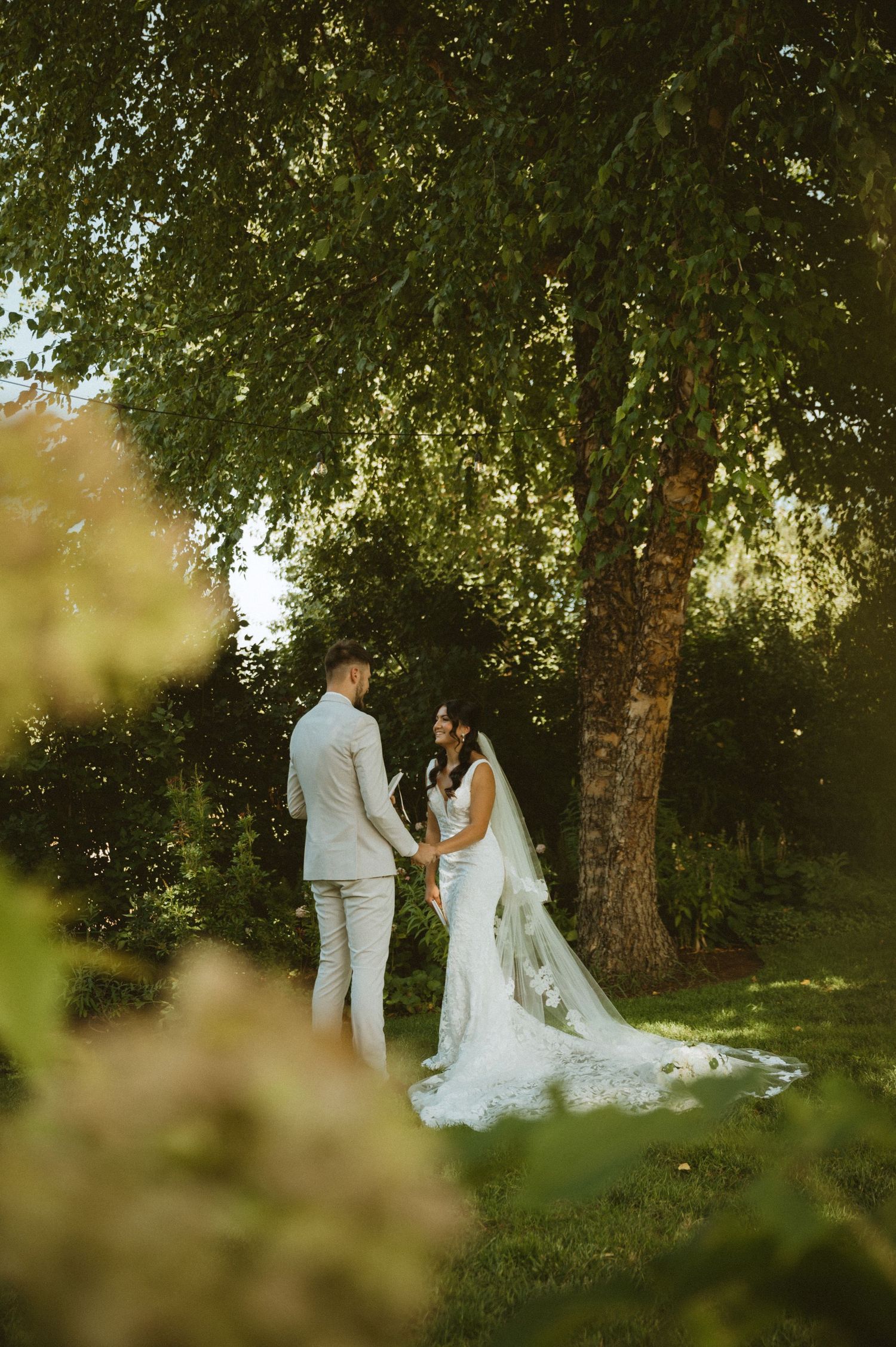 Bride and groom sharing intimate moment under tree canopy in natural setting.