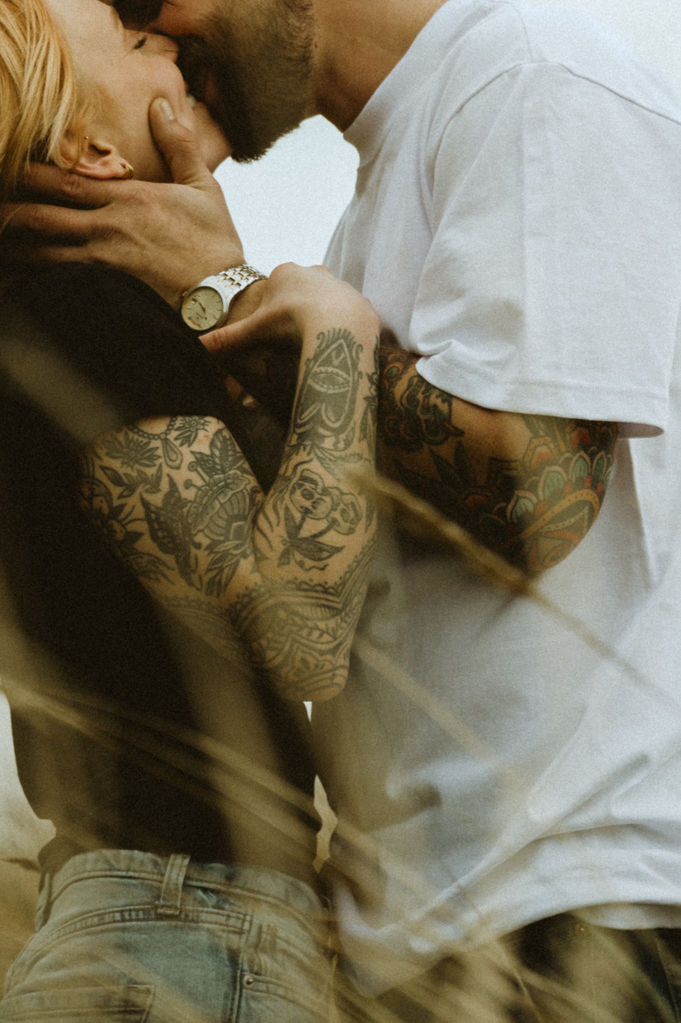 Close-up of tattooed arms in casual clothing against a warm-toned background.
