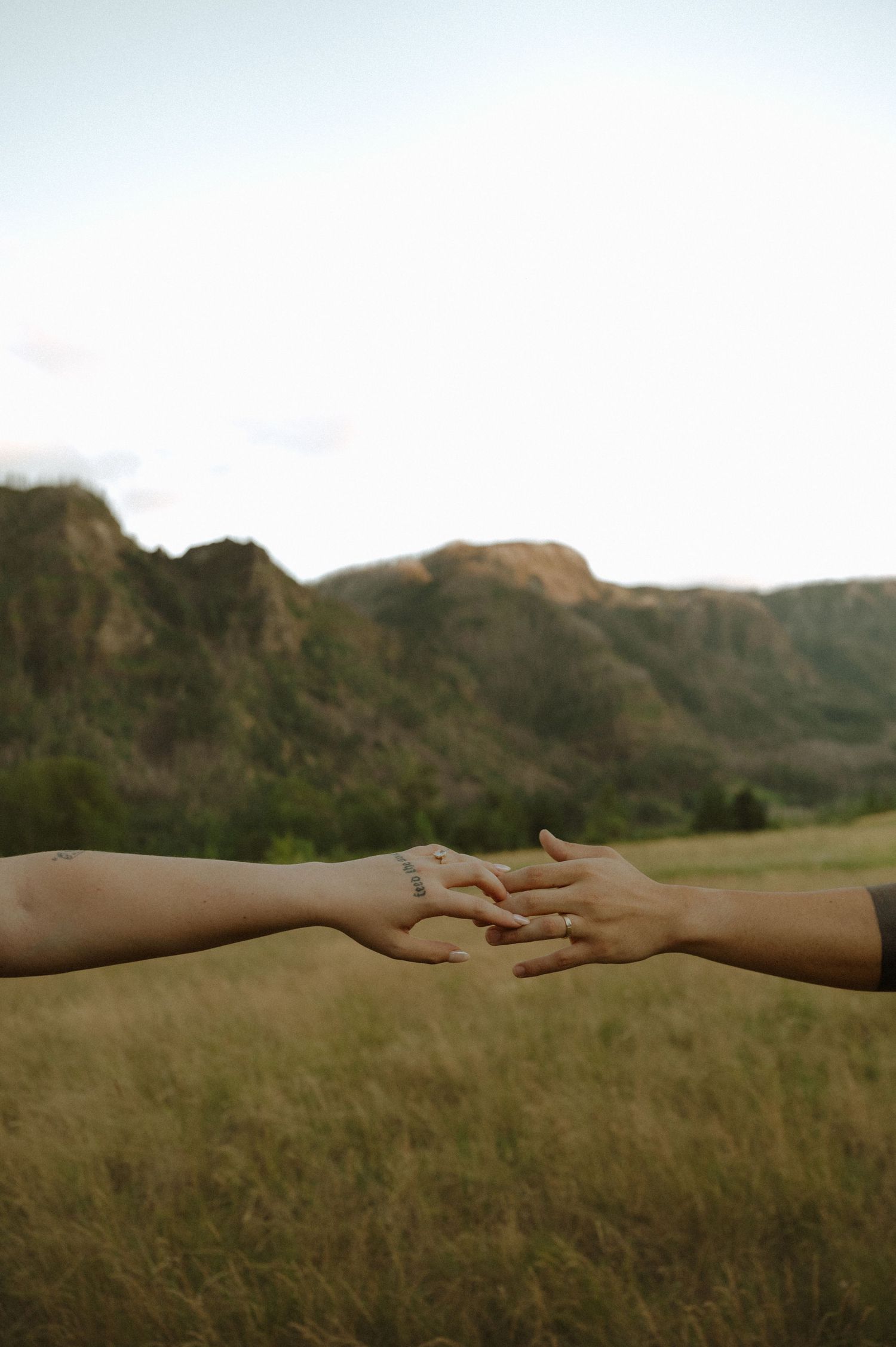 Two hands reaching towards each other against a scenic mountain landscape backdrop at sunset.