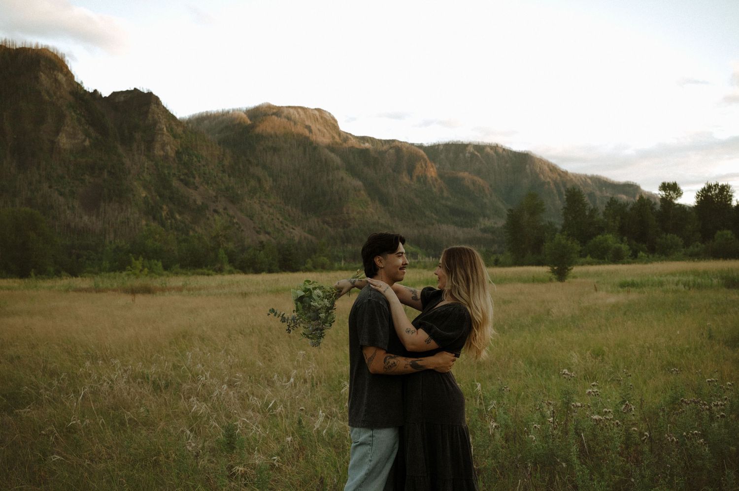 Couple embracing in mountain field during golden hour.