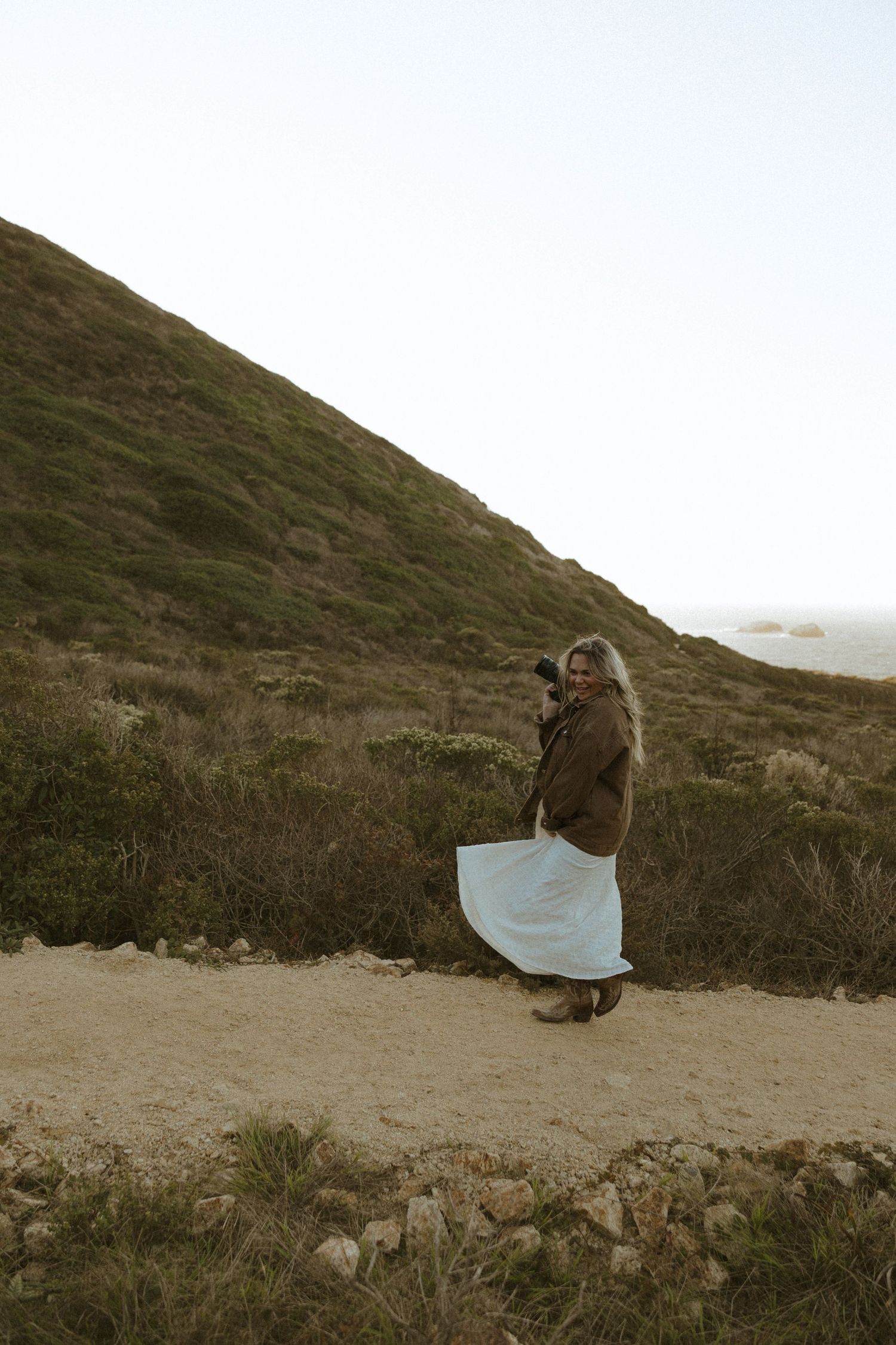 Figure in casual attire photographing on hillside terrain at dusk.