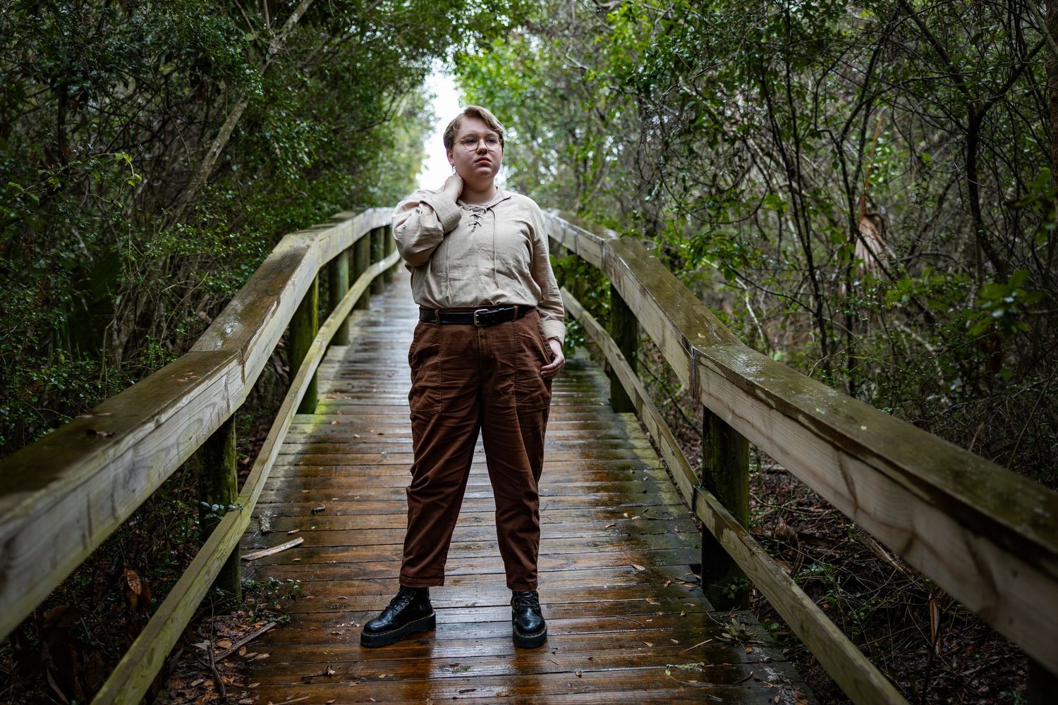 Figure standing centered on a wooden boardwalk path through dense green foliage.