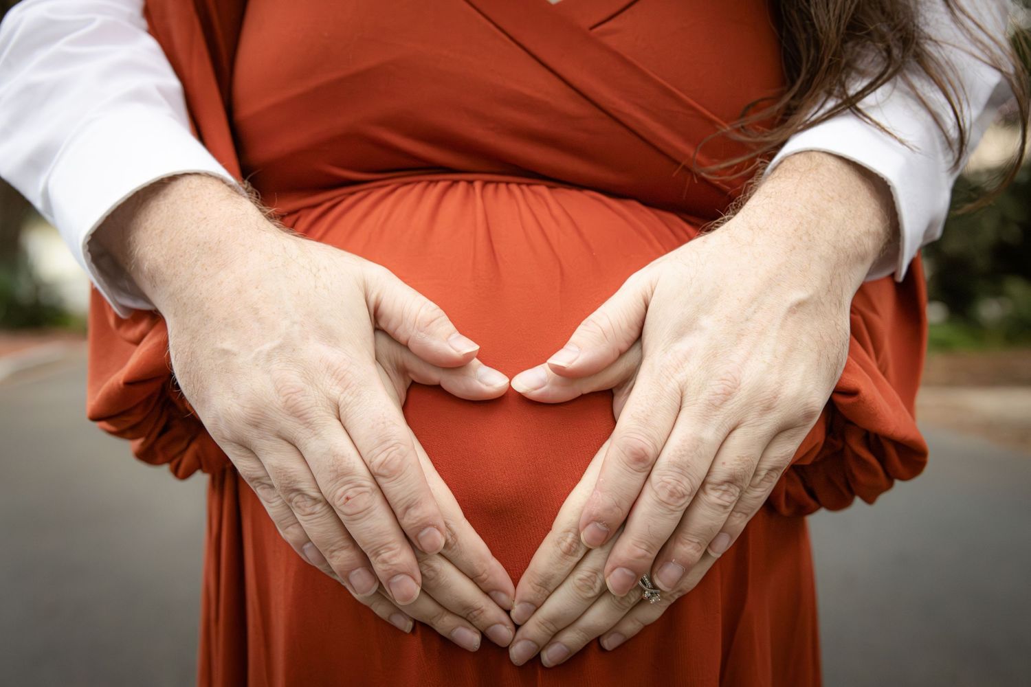 Hands forming a heart shape over a pregnant belly in a red dress.