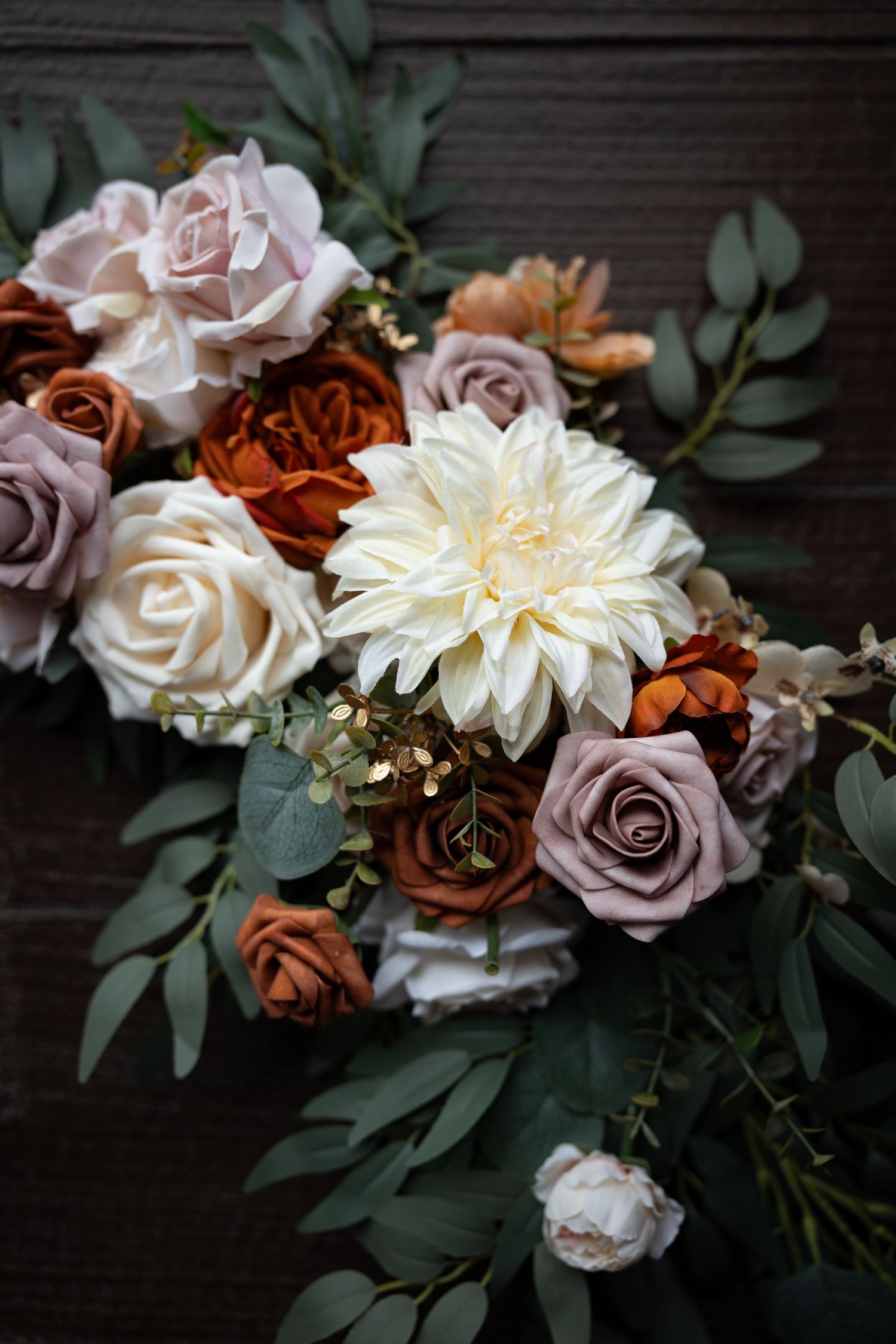 Elegant floral arrangement with roses and dahlias in muted pink and burgundy tones on dark wood.