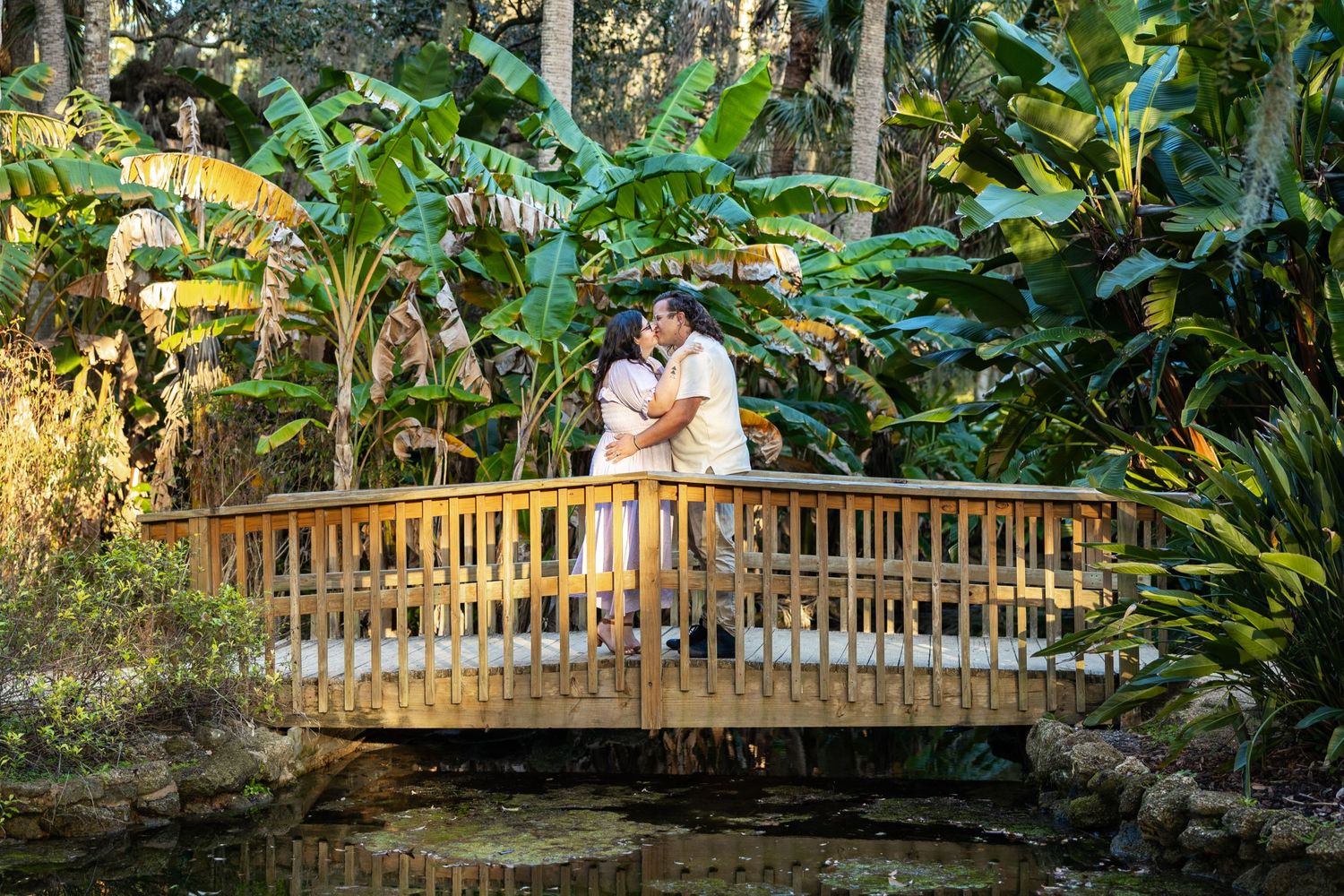 A couple sharing an intimate moment on a wooden bridge in a tropical garden.