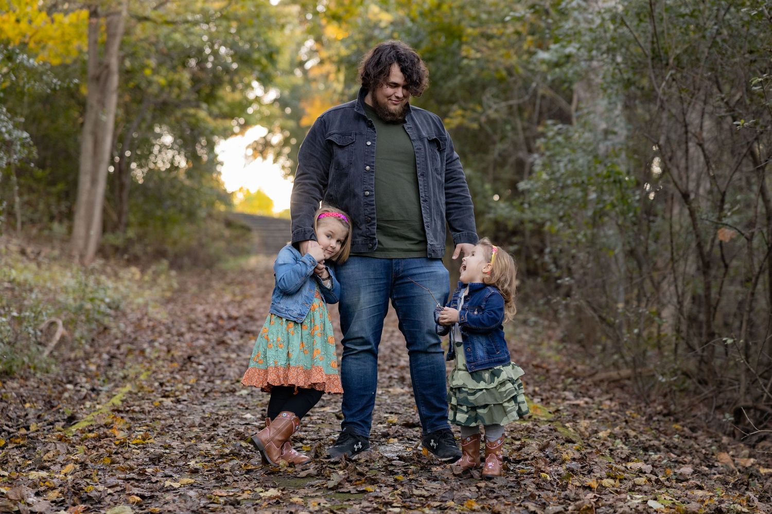 Family portrait on an autumn trail surrounded by fallen leaves and trees.