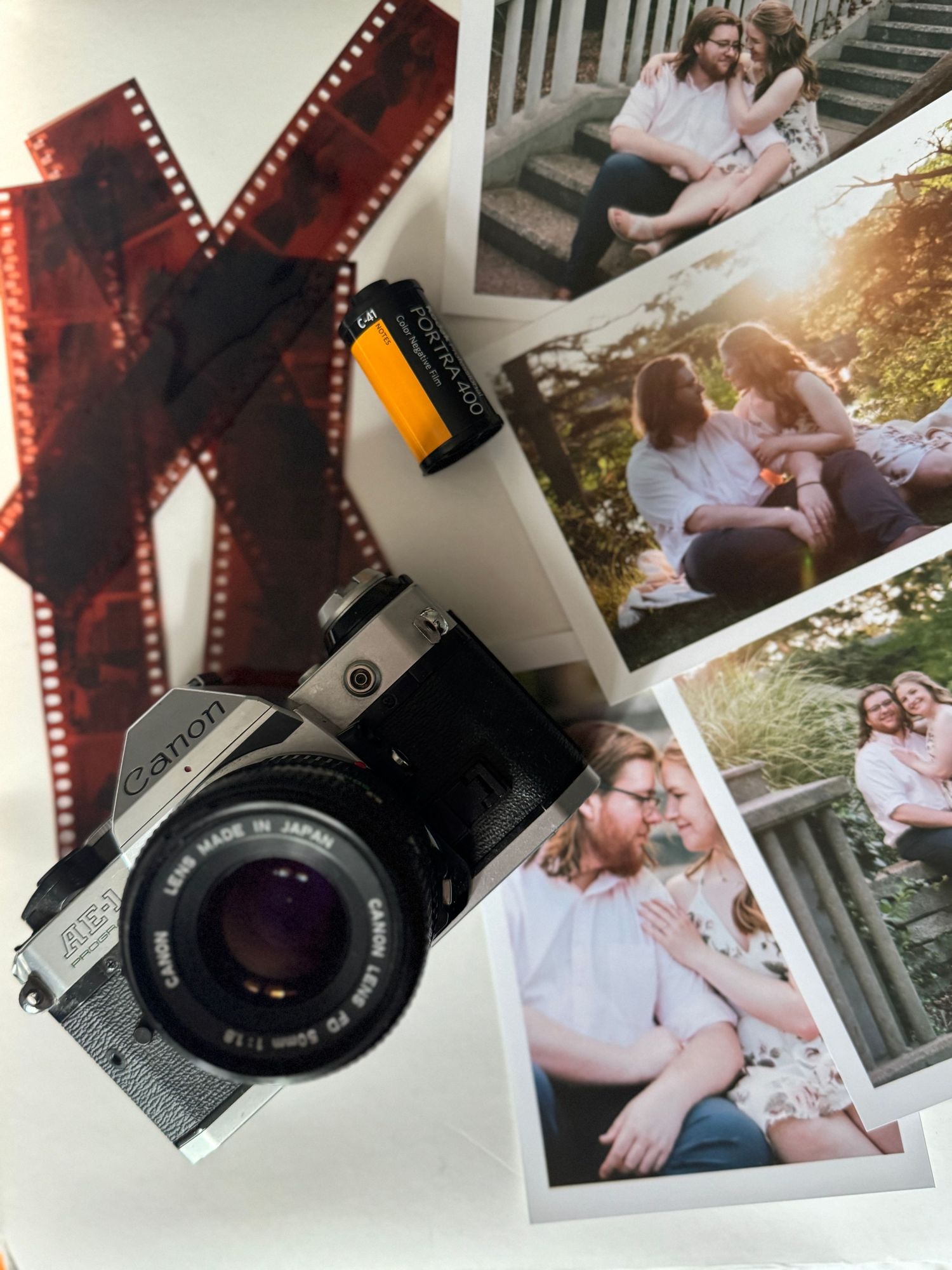 Vintage camera film strips and developed photographs scattered on a white surface with a retro camera in view.