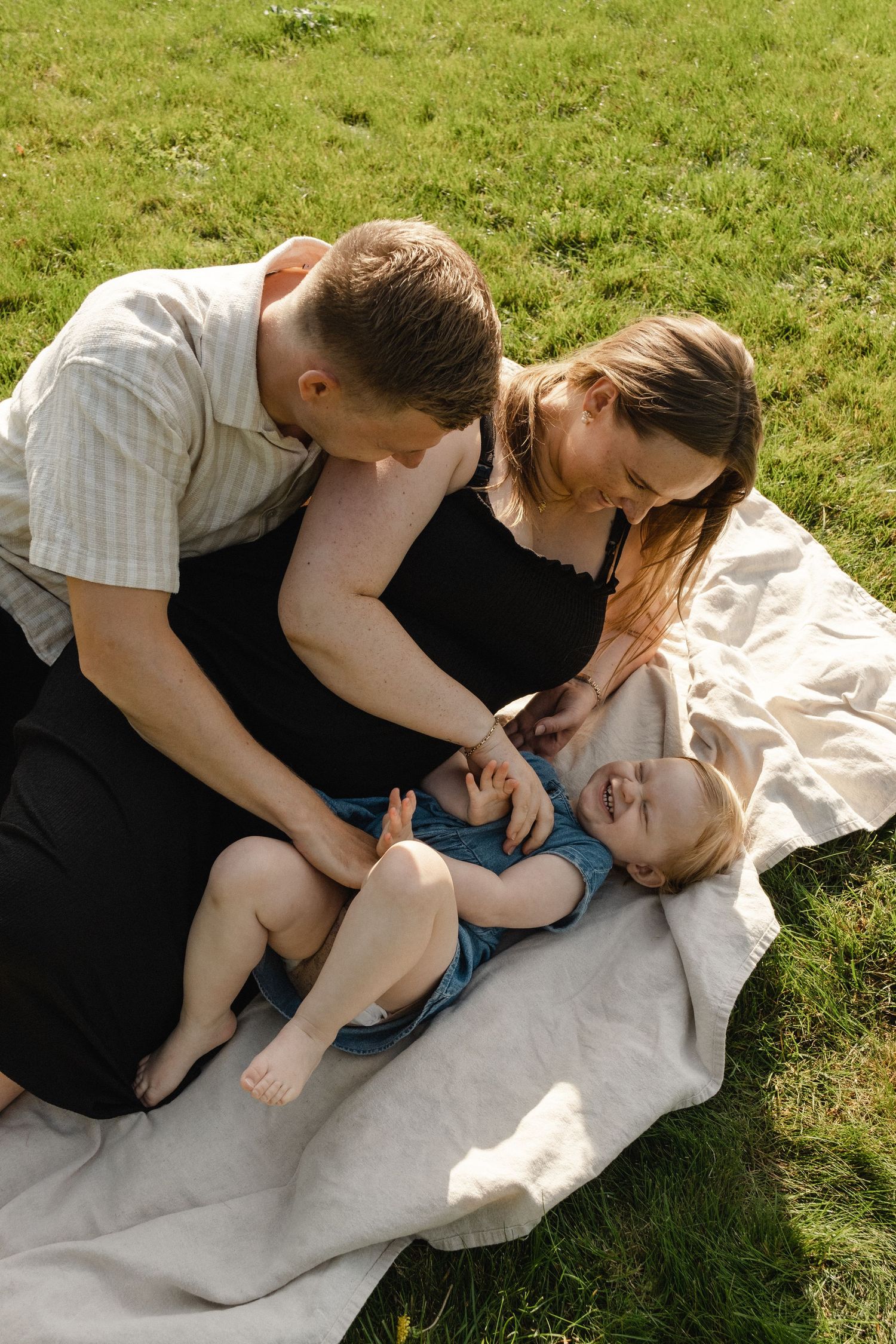 Family sharing tender moments while relaxing on blanket in sunny grassland.