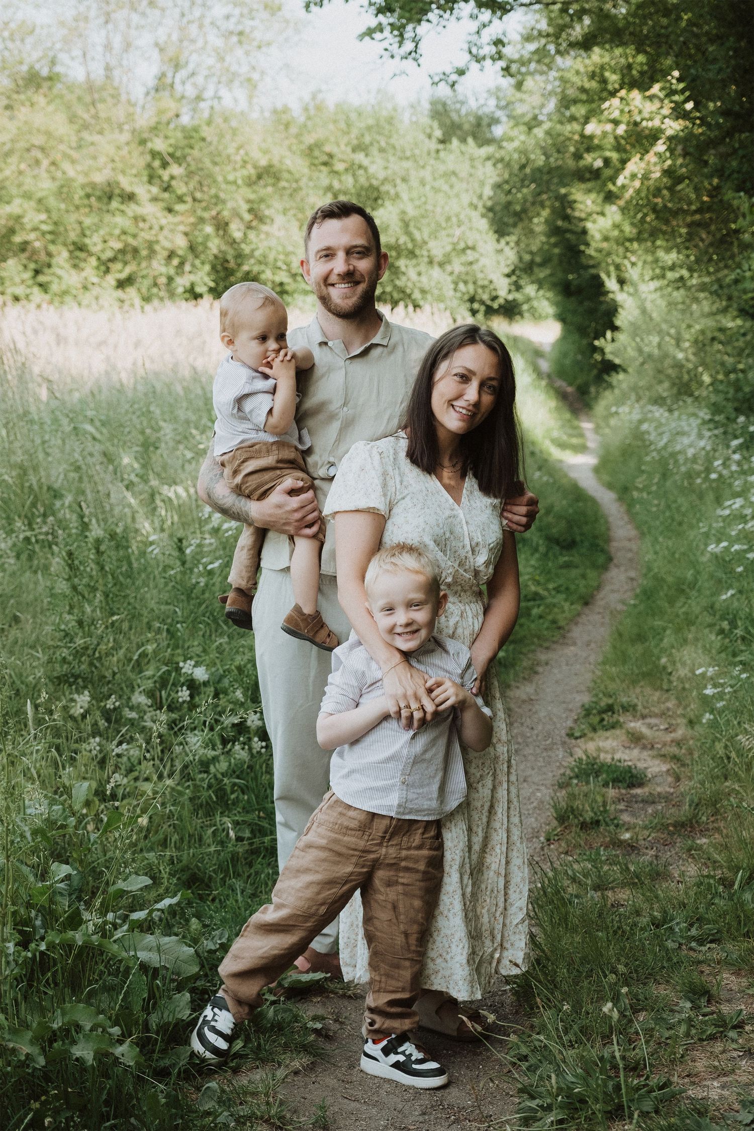 Happy family of four poses together on a nature trail surrounded by greenery.