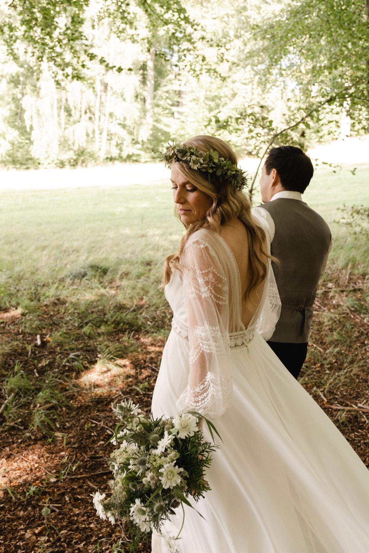 A romantic woodland wedding scene with a bride in a delicate lace gown holding a white bouquet.