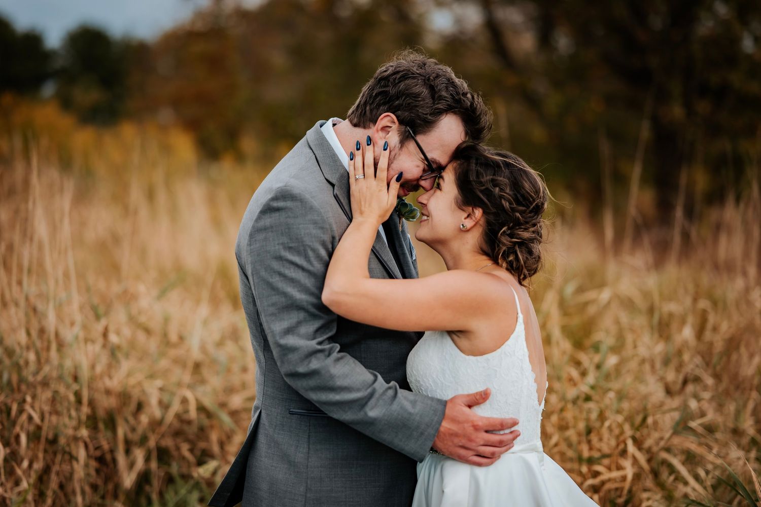 A couple shares a romantic almost-kiss in a golden autumn field, bride in white dress and groom in gray suit.
