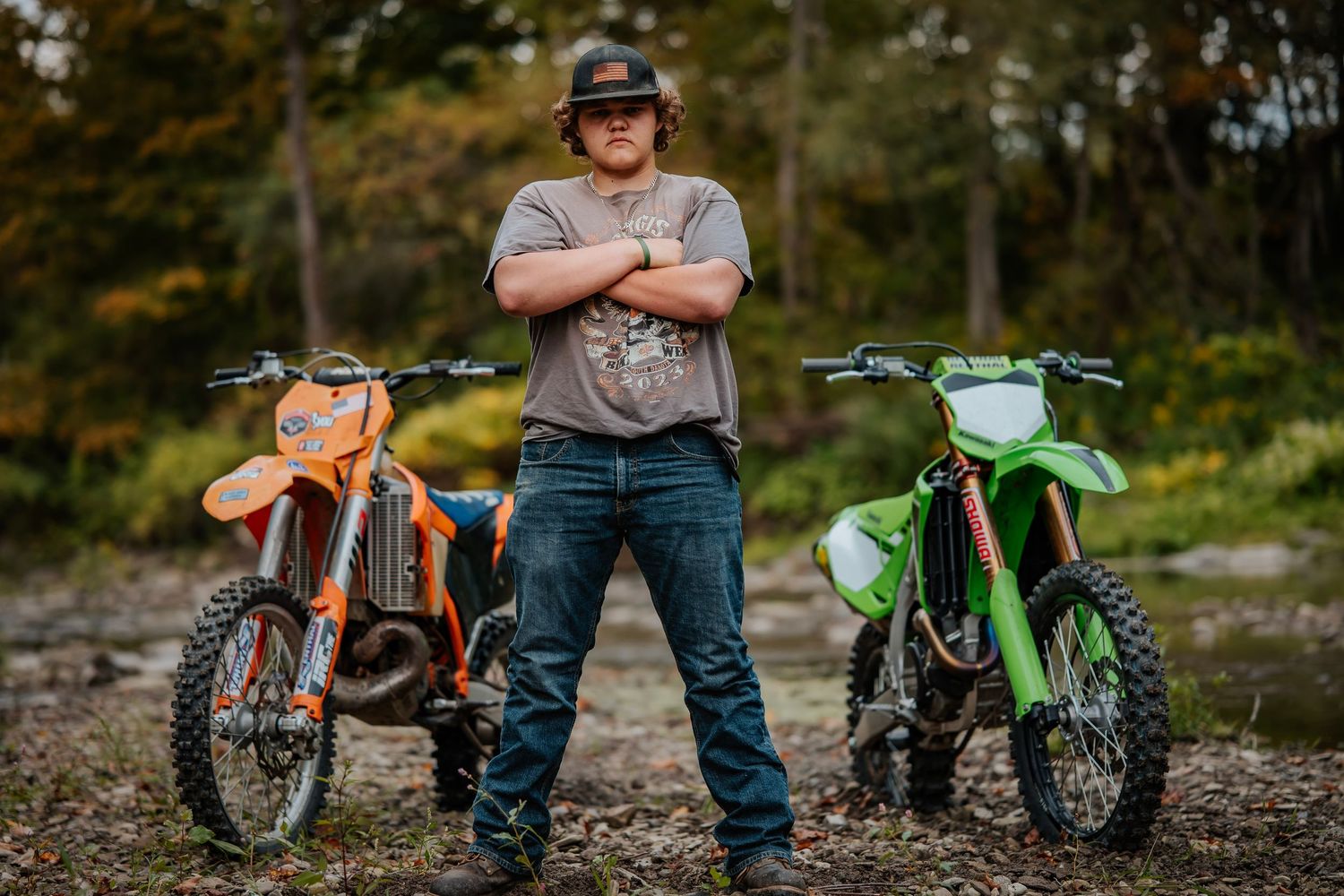 A series of vintage and modern dirt bikes parked in a row against a natural outdoor background.