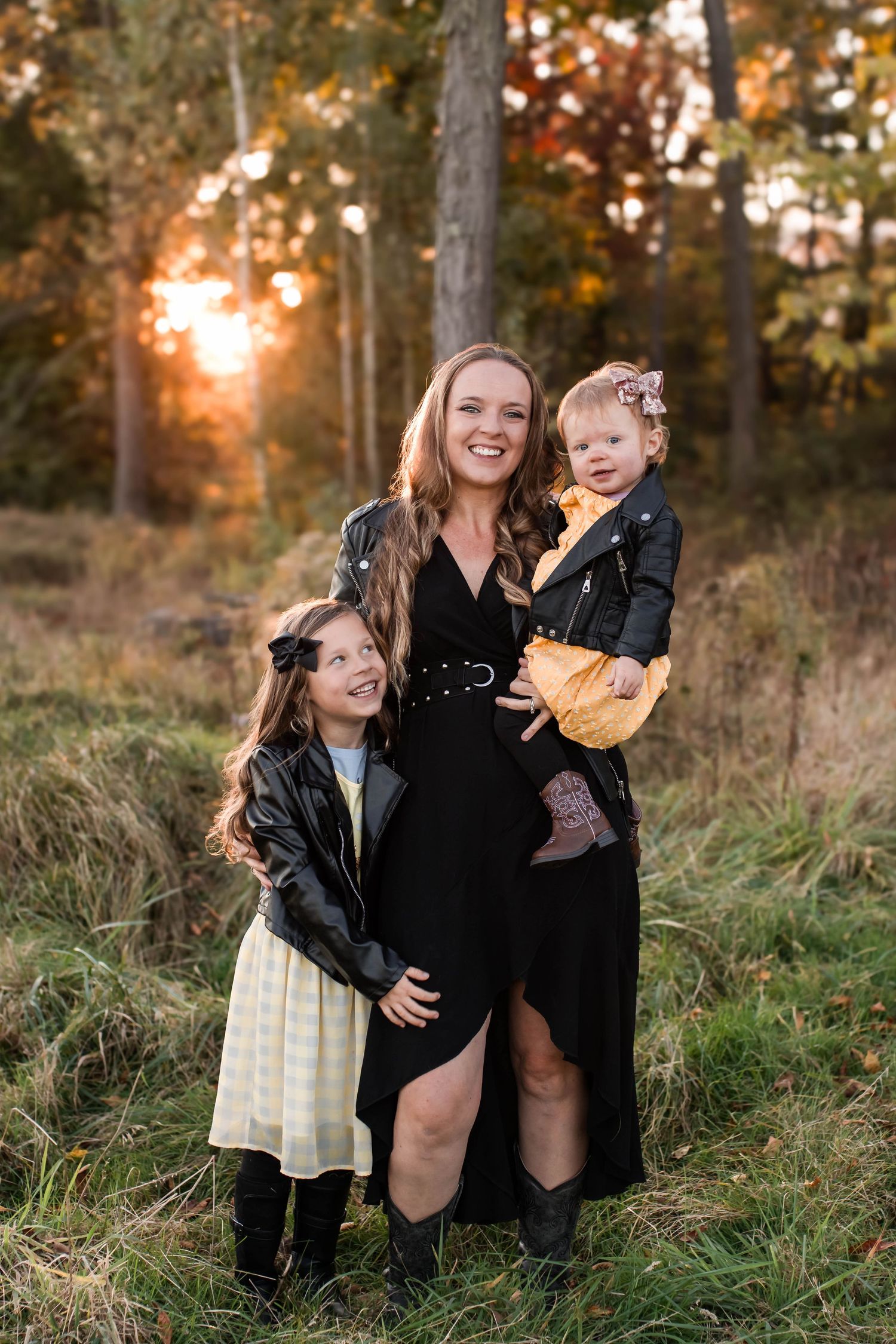 A family enjoys a playful moment together in a sunlit autumn field with tall grass and trees in the background.