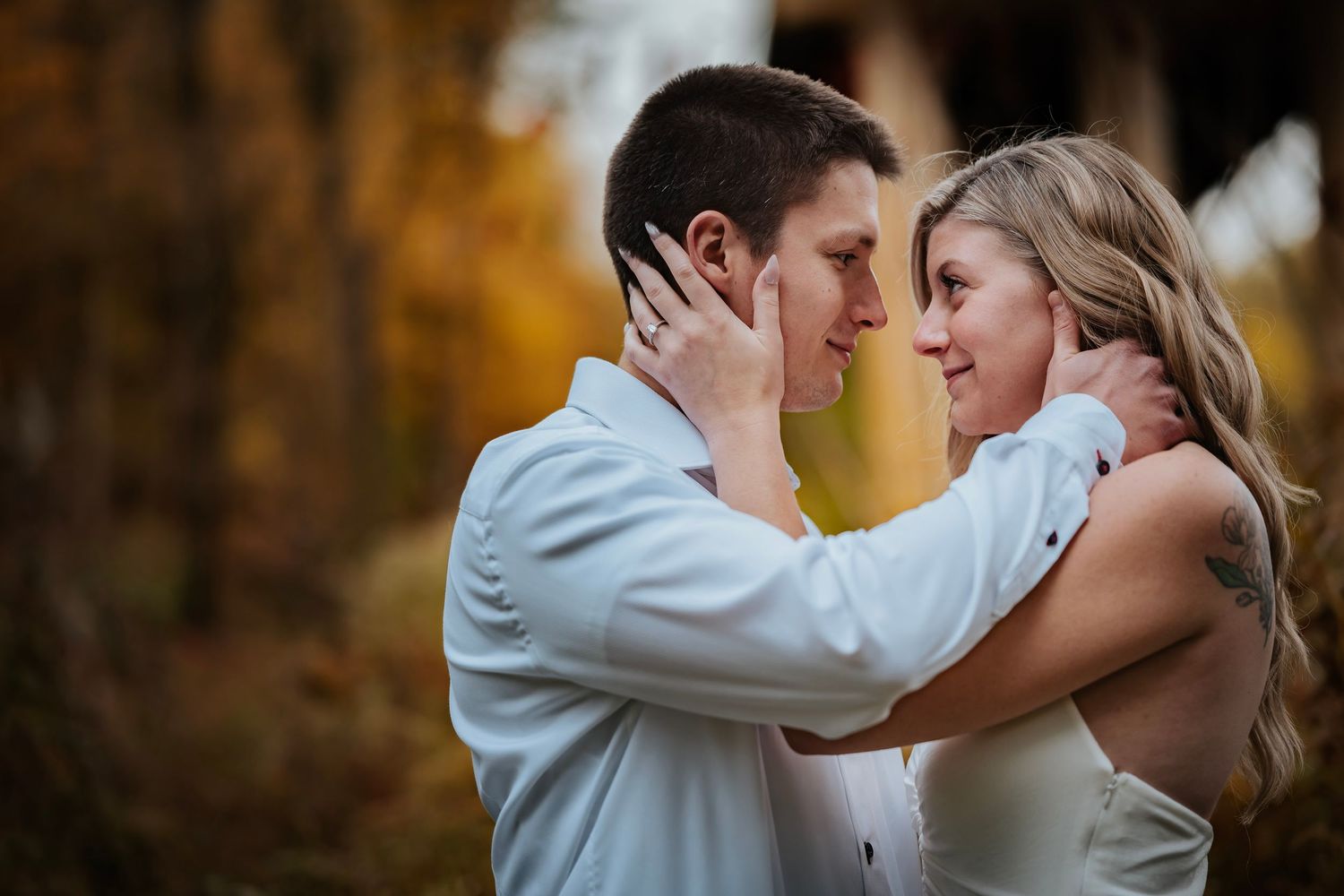A couple in wedding attire shares a romantic moment outdoors surrounded by golden autumn foliage.