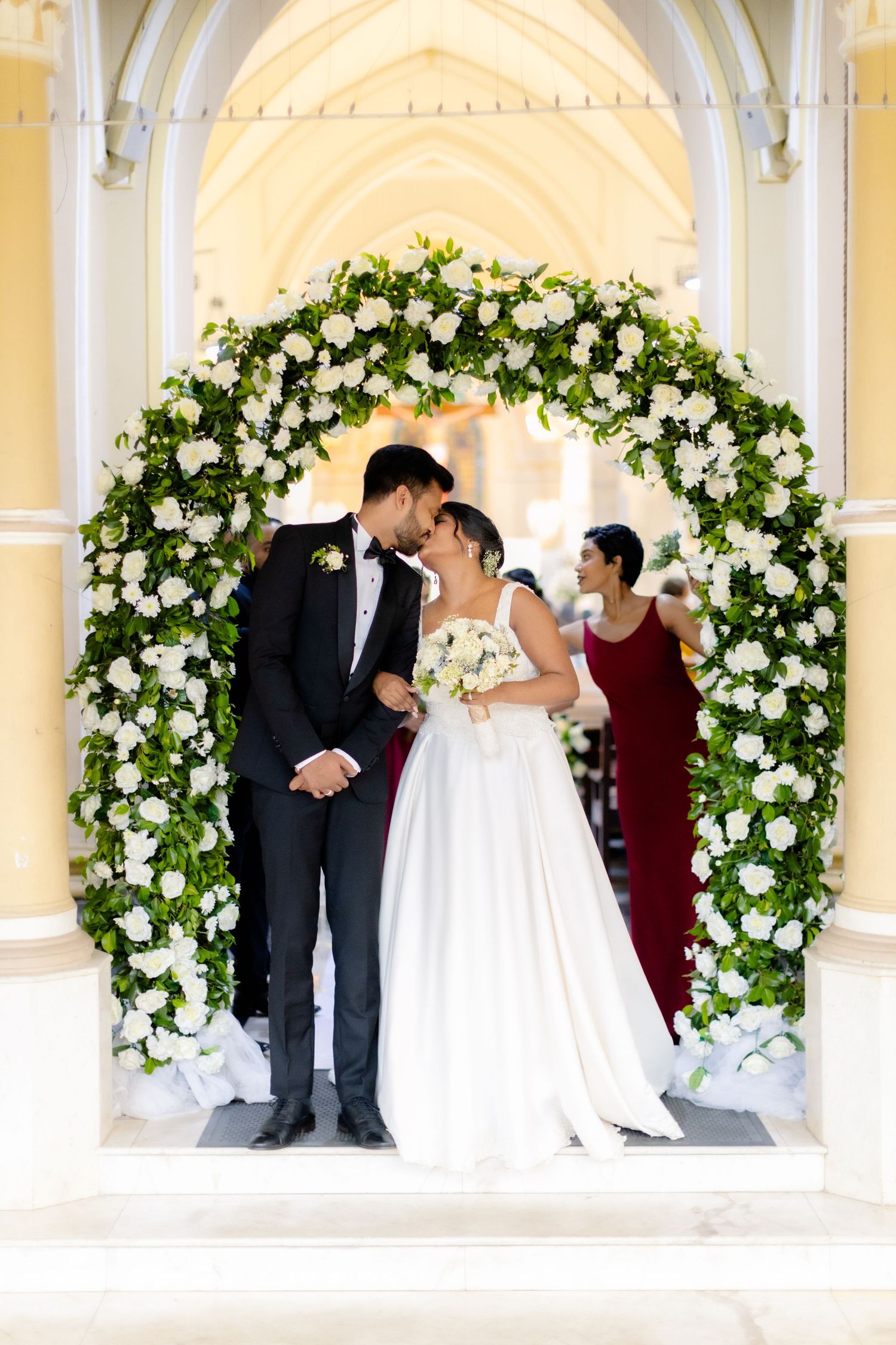 Wedding ceremony under beautiful white floral arch with gothic architectural details.