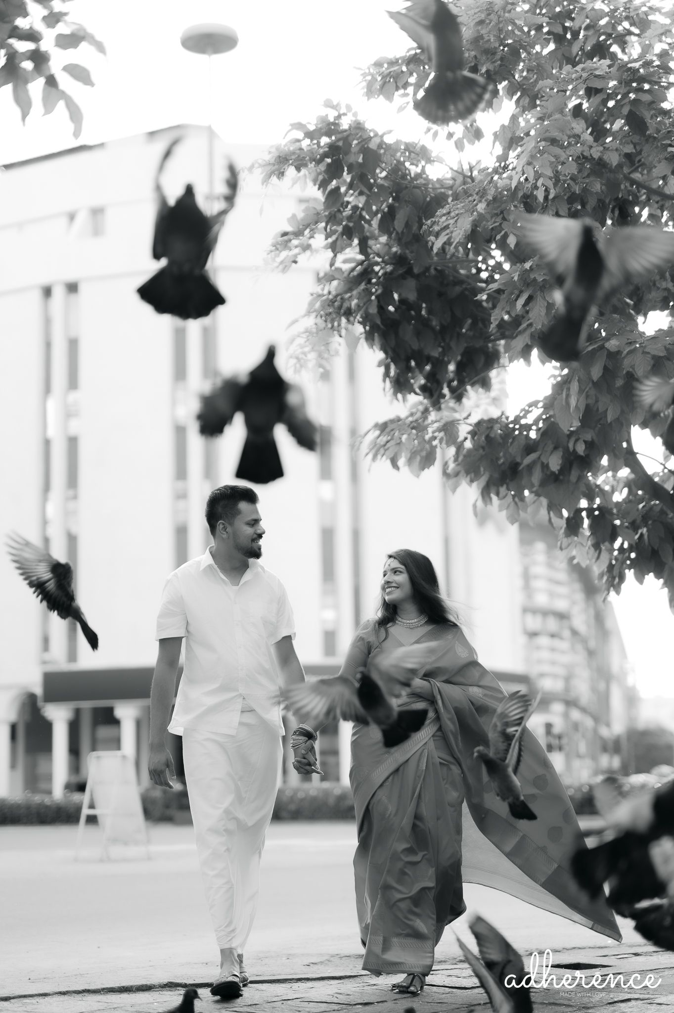 Couple in white outfits walking together with flying birds in black and white photography.