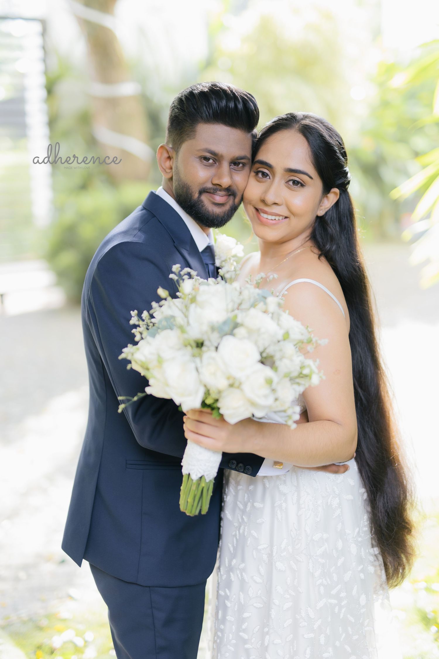 Newlyweds pose with white bouquet, bride in lace gown and groom in navy suit.