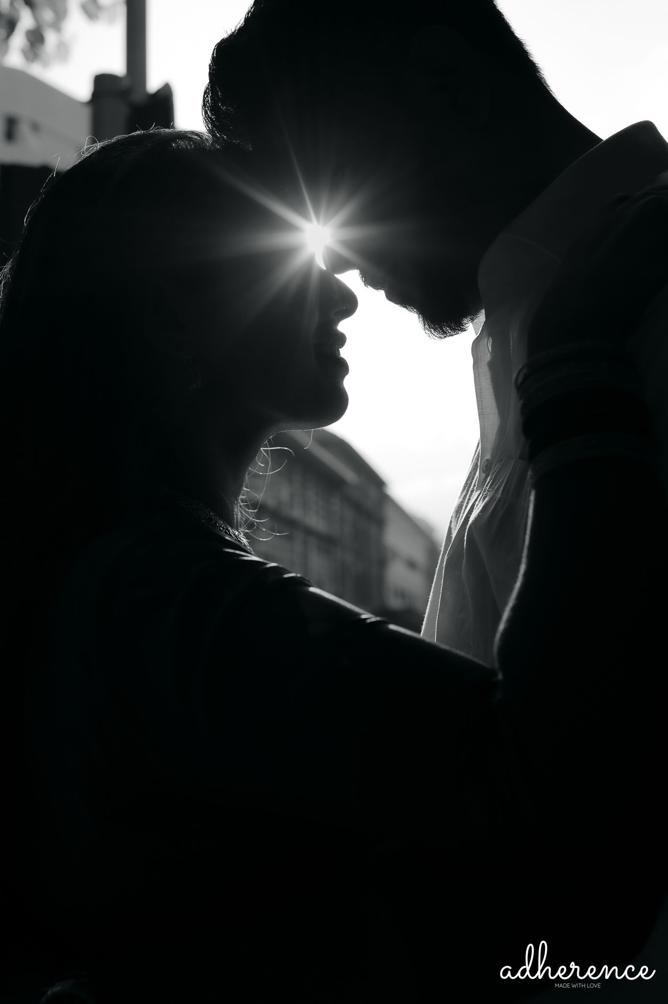 Romantic silhouette of a couple in an intimate moment with sunburst between them in black and white.
