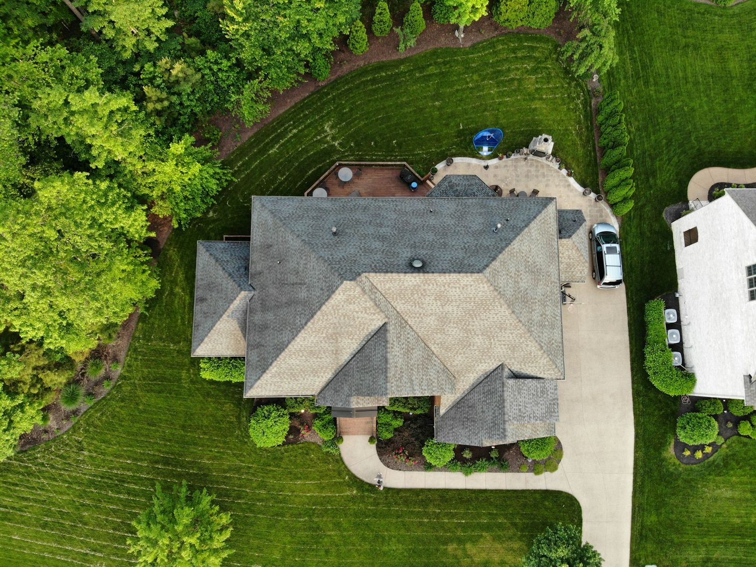 Aerial view of a large suburban home with gray roof surrounded by lush green trees and manicured lawn.
