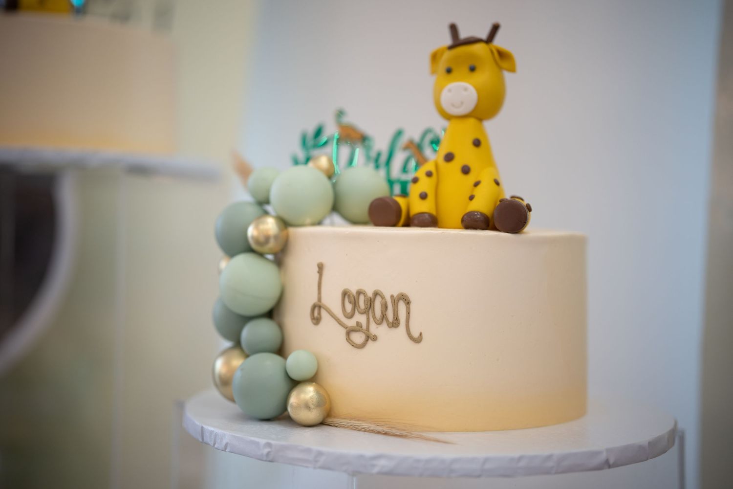 White birthday cake with giraffe topper and balloon decorations personalized with the name Logan.