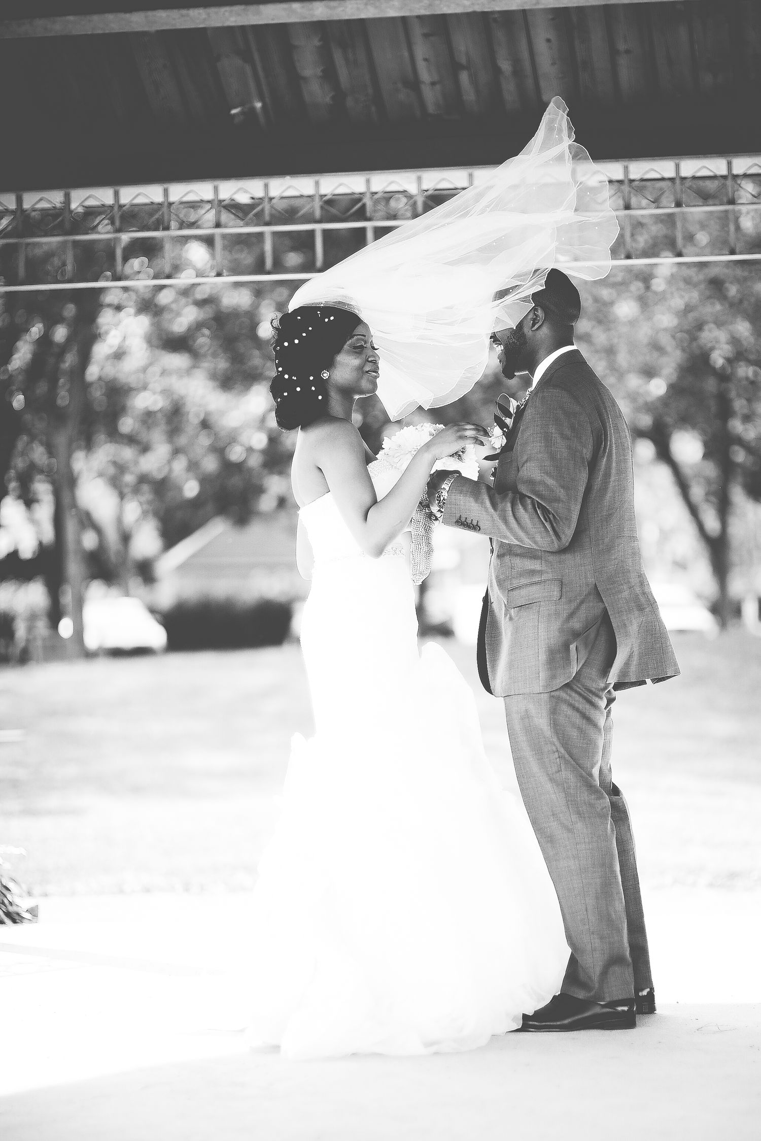 Black and white photo of bride and groom dancing outdoors, brides veil flowing in the wind.