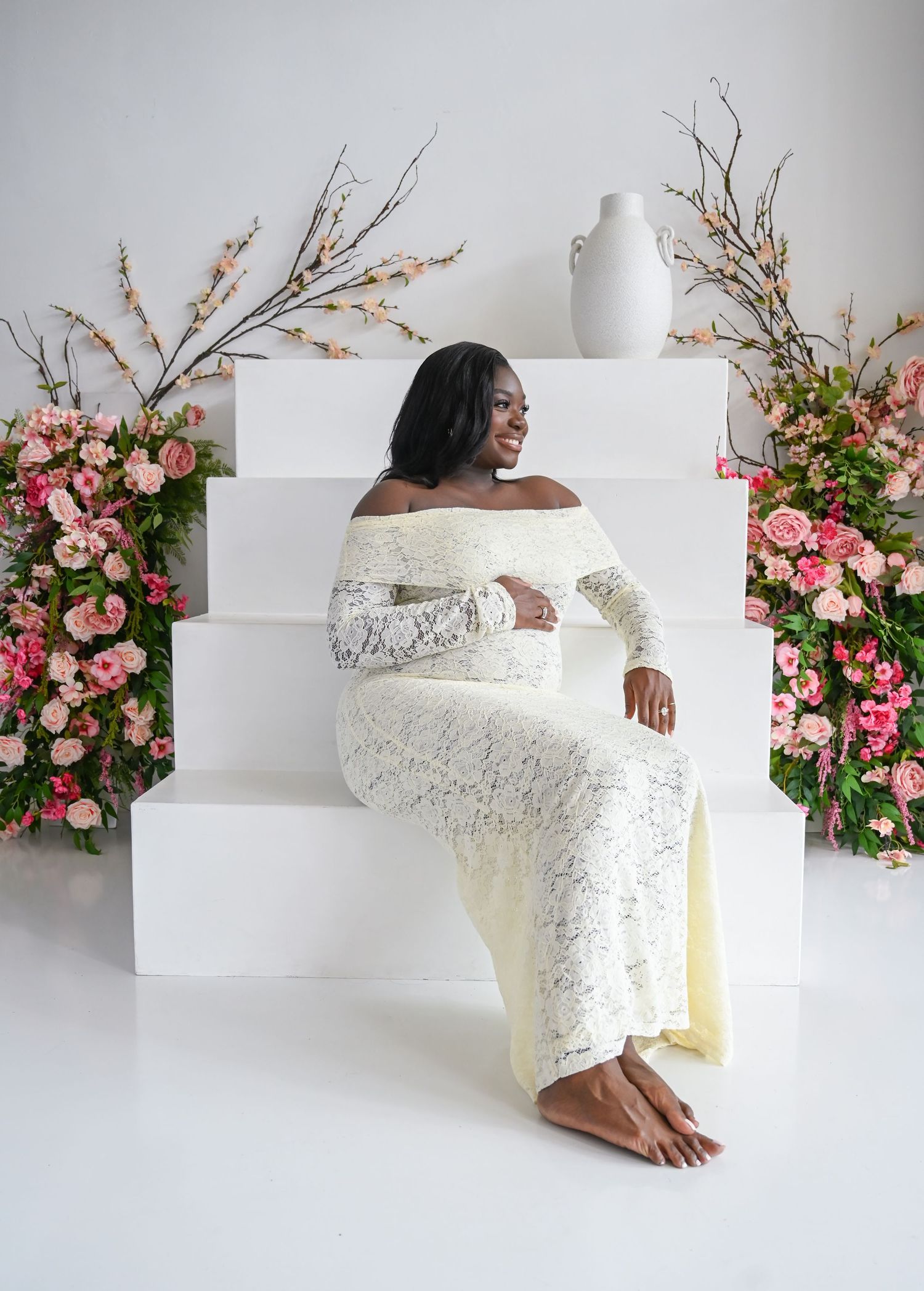 A series of artistic photos showing a white lace wedding dress against a white backdrop with pink floral arrangements.