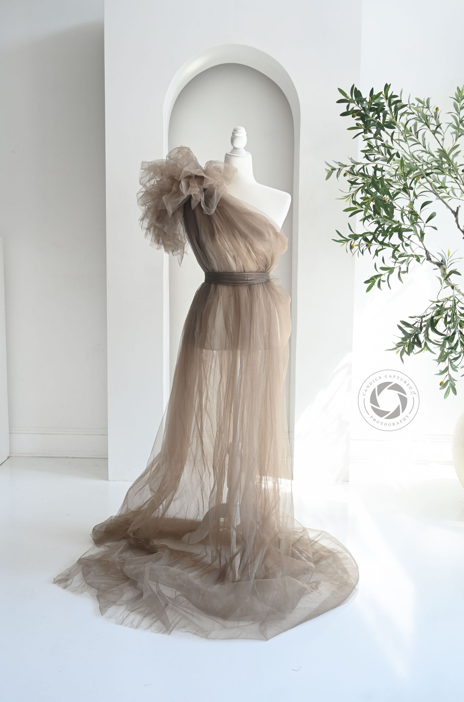 Ethereal dusty rose tulle maternity gown with ruffled neckline displayed on mannequin against white backdrop.
